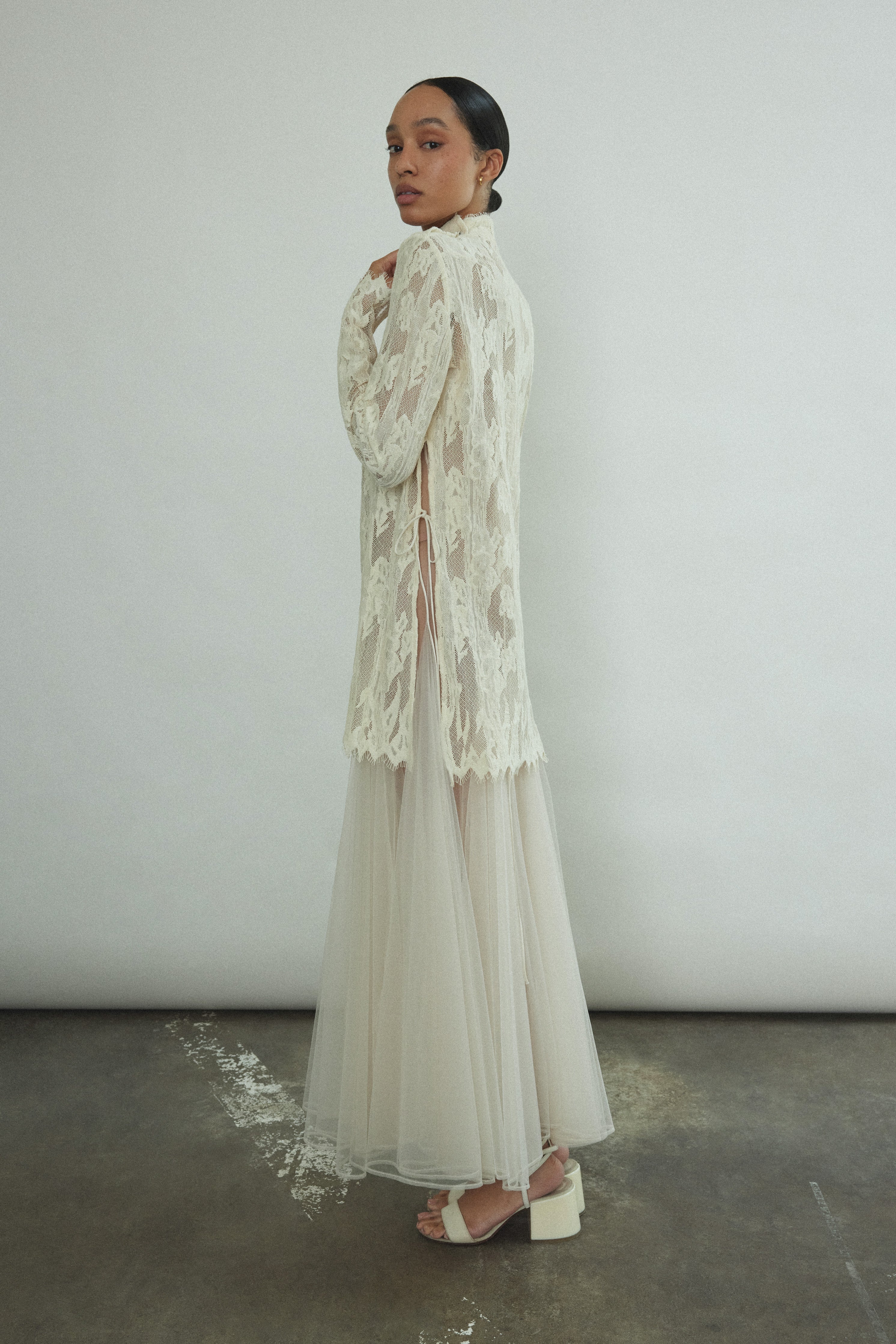 Kamperett Isabella Tunic in cream French lace, full-length side view showing straight-cut silhouette, mock neck, eyelash lace hem, and long sleeves with wrist zipper closure.