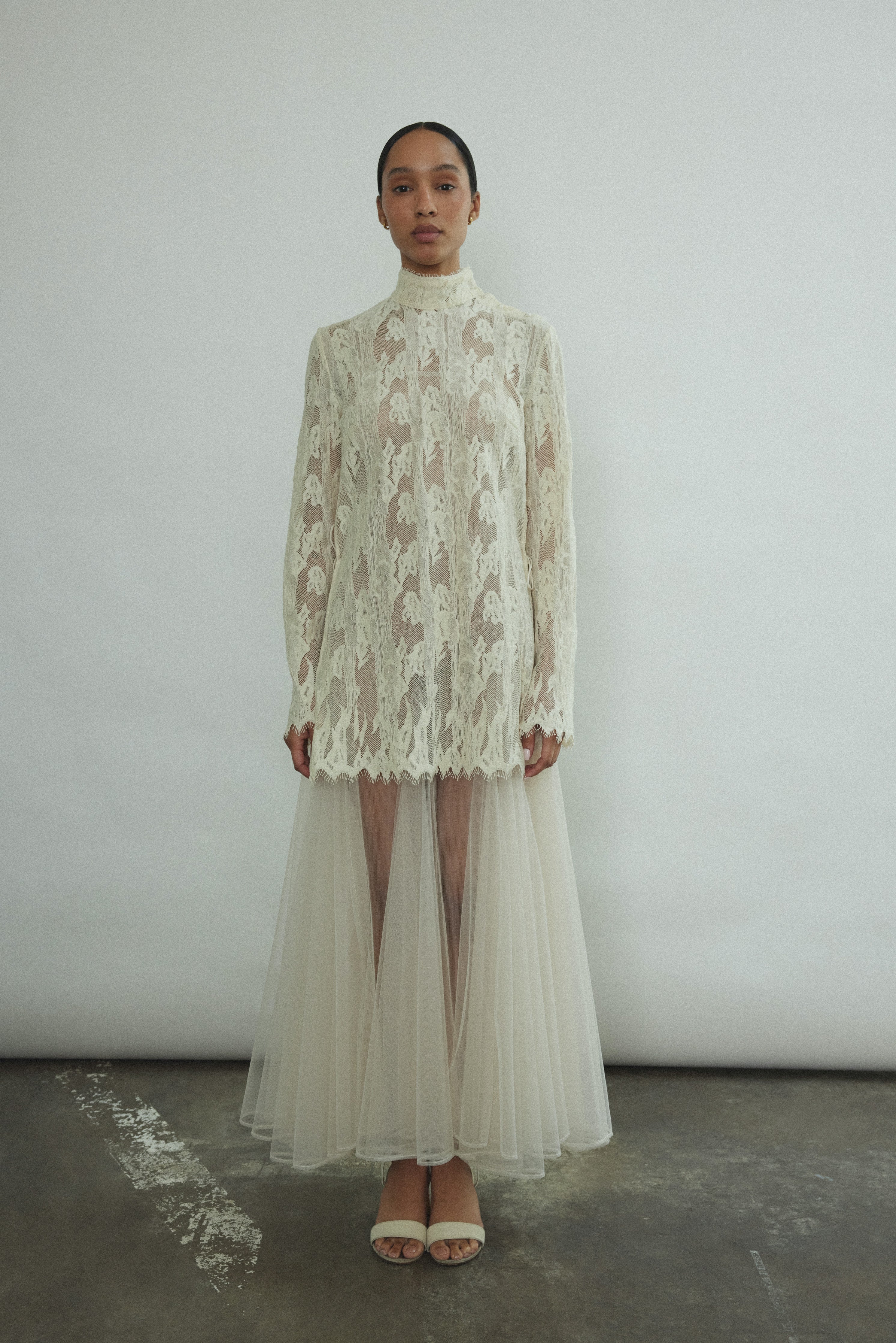 Kamperett Isabella Tunic in cream French lace, full-length front view showing straight-cut silhouette, mock neck, eyelash lace hem, and long sleeves with wrist zipper closure.