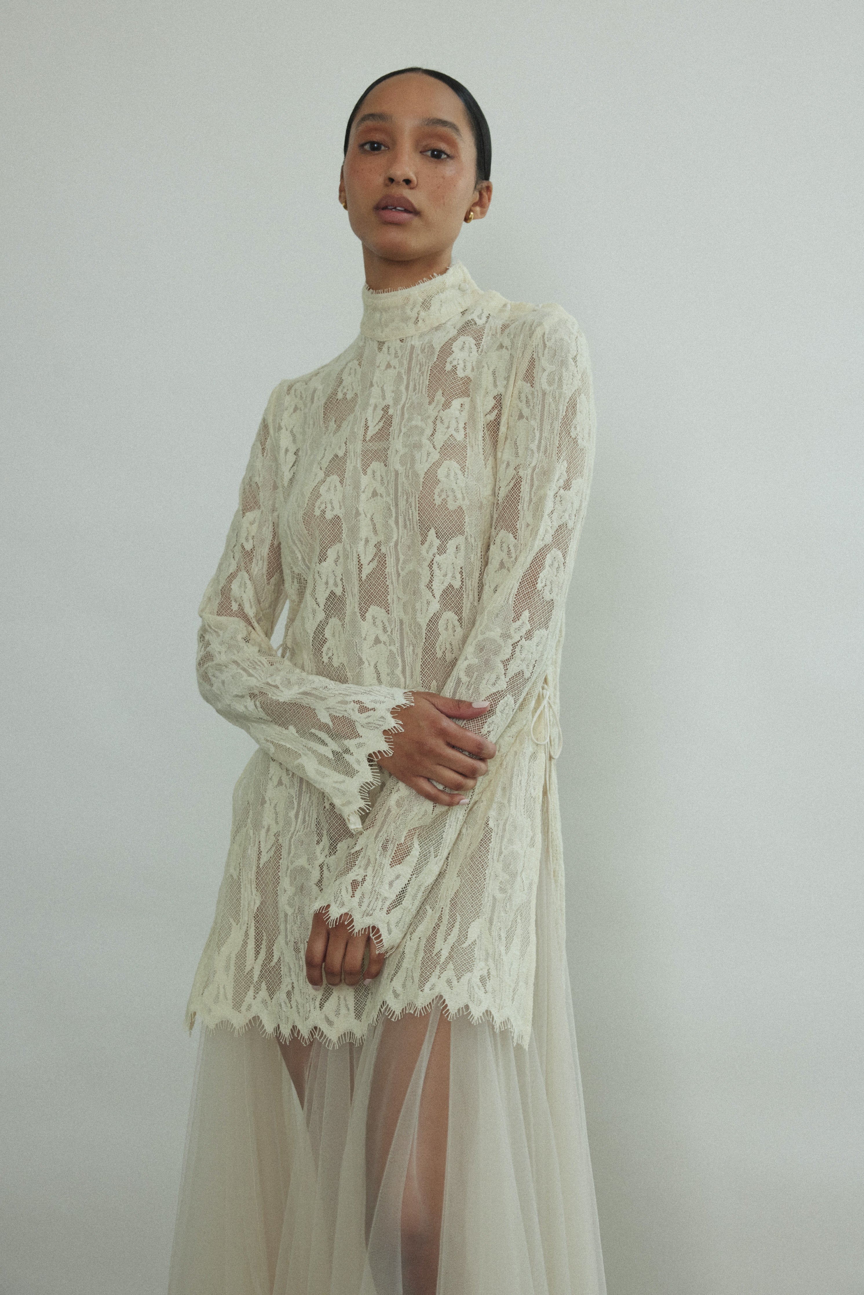 Cream French lace tunic, straight-cut silhouette, mock neck, long sleeves with eyelash lace hem. Minimalist occasionwear made in California.
