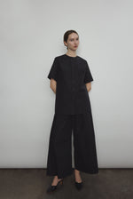 Front view of a model wearing the black Japanese cotton lawn Kamperett Jette Tee, an oversized reversible top with wide button placket.