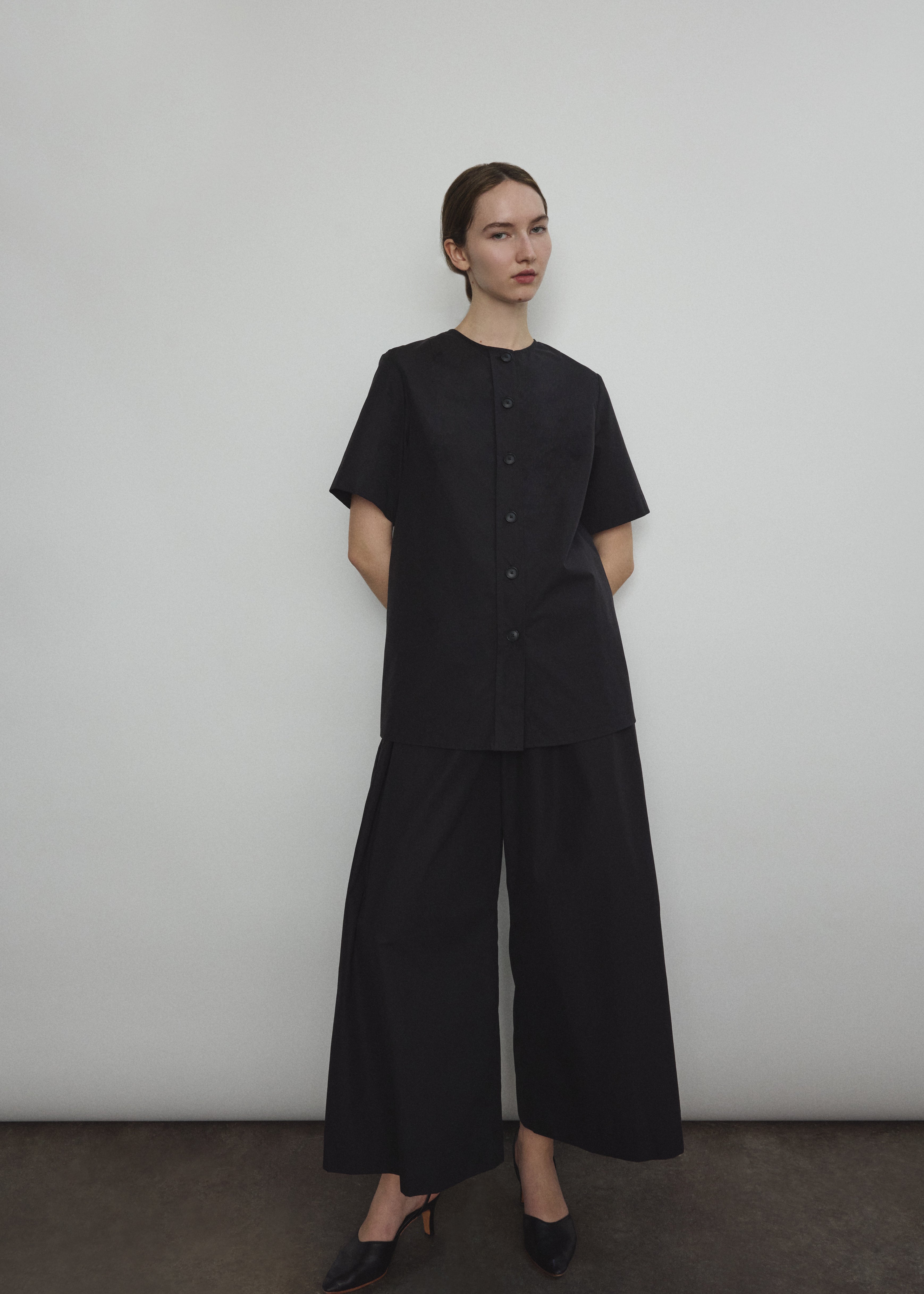 Front view of a model wearing the black Japanese cotton lawn Kamperett Jette Tee, an oversized reversible top with wide button placket.