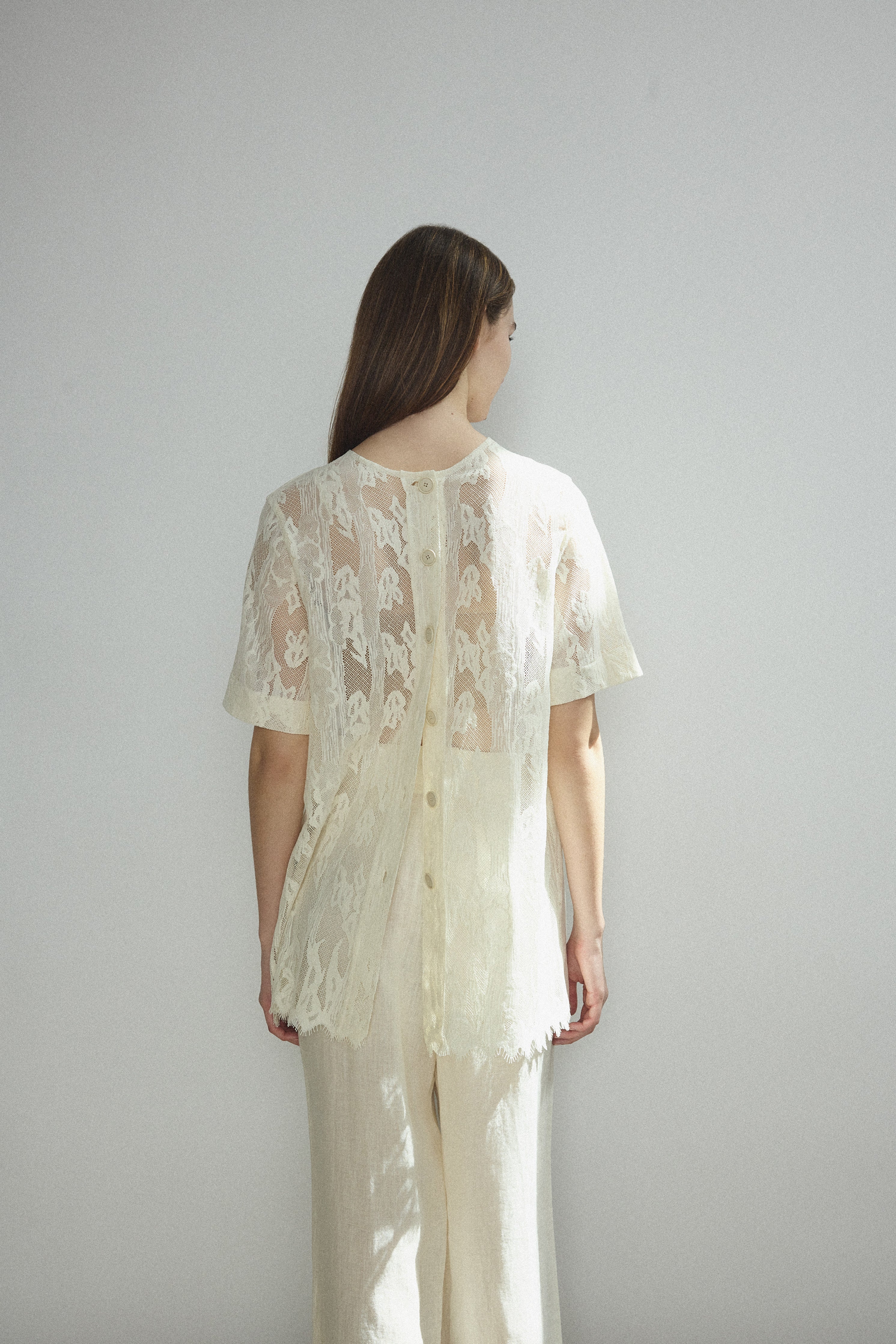 Motion shot of the cream French lace Kamperett Jette Tee, capturing the fluid drape.