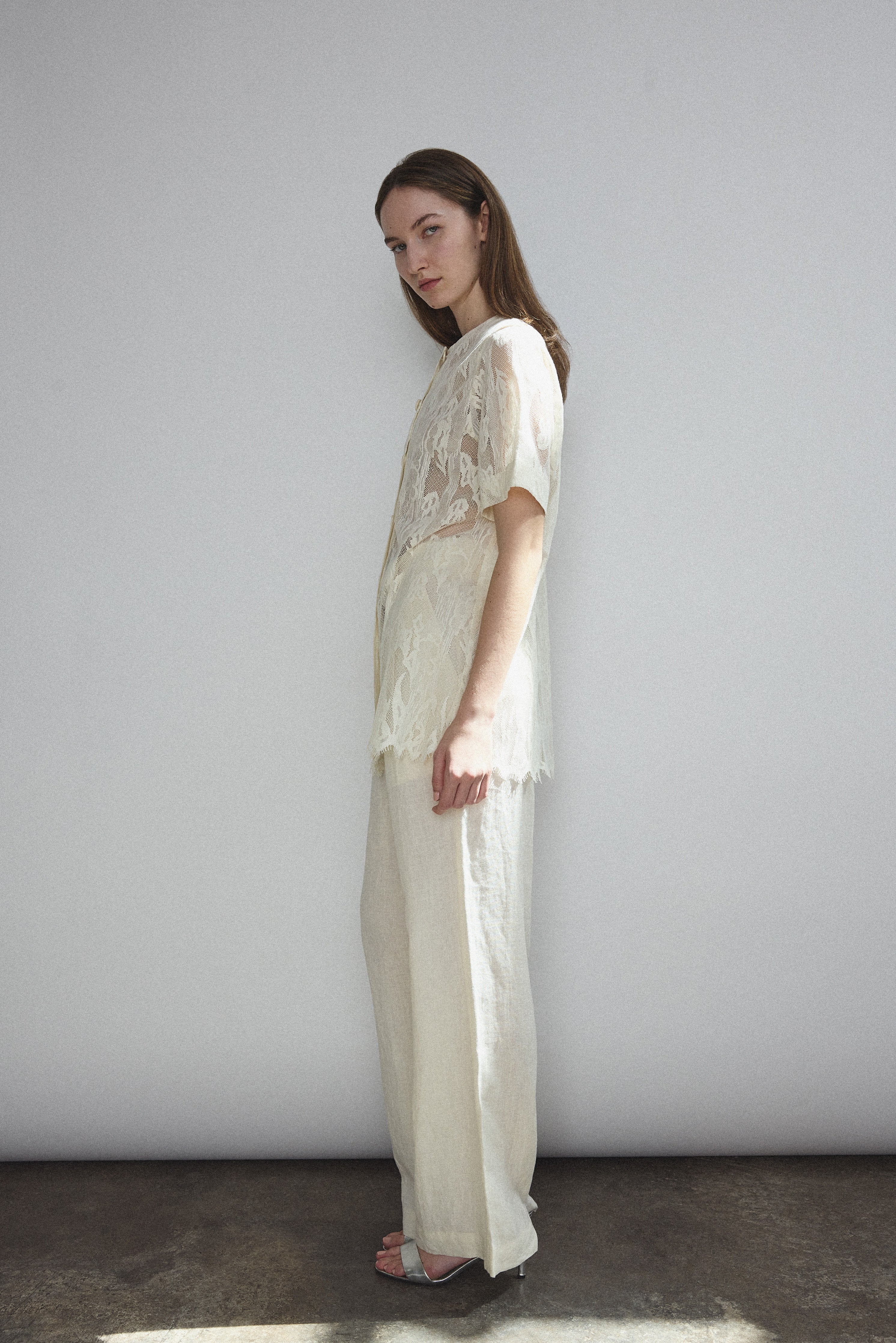 Angled view of the cream French lace Kamperett Jette Tee styled with the Huene Pant.