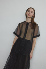 Front view of a model wearing the black silk organza Kamperett Jette Tee, an oversized reversible top with wide button placket.