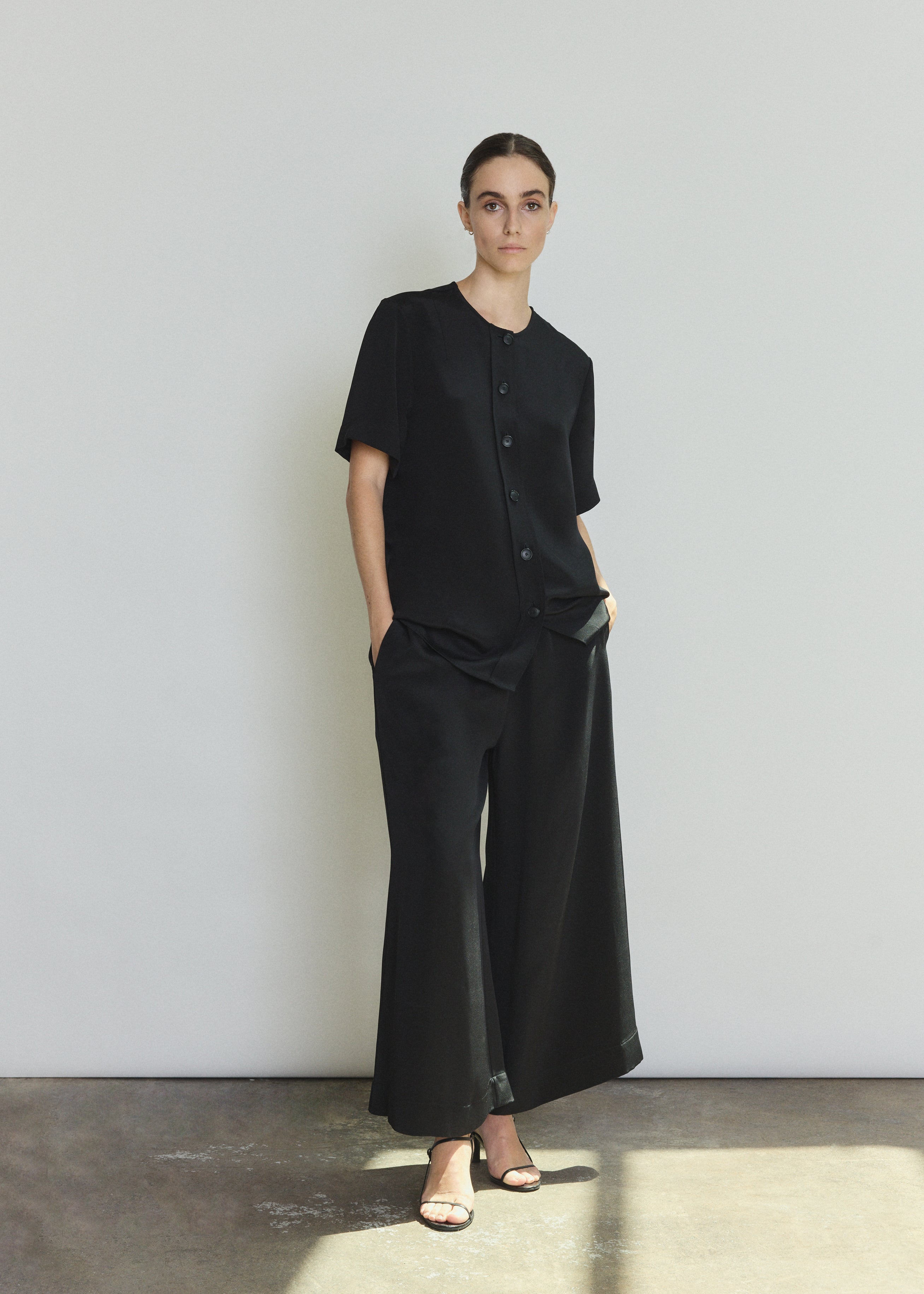 Front view of a model wearing the black silk crepe Kamperett Jette Silk Crepe Tee, an oversized reversible tee with wide button placket.