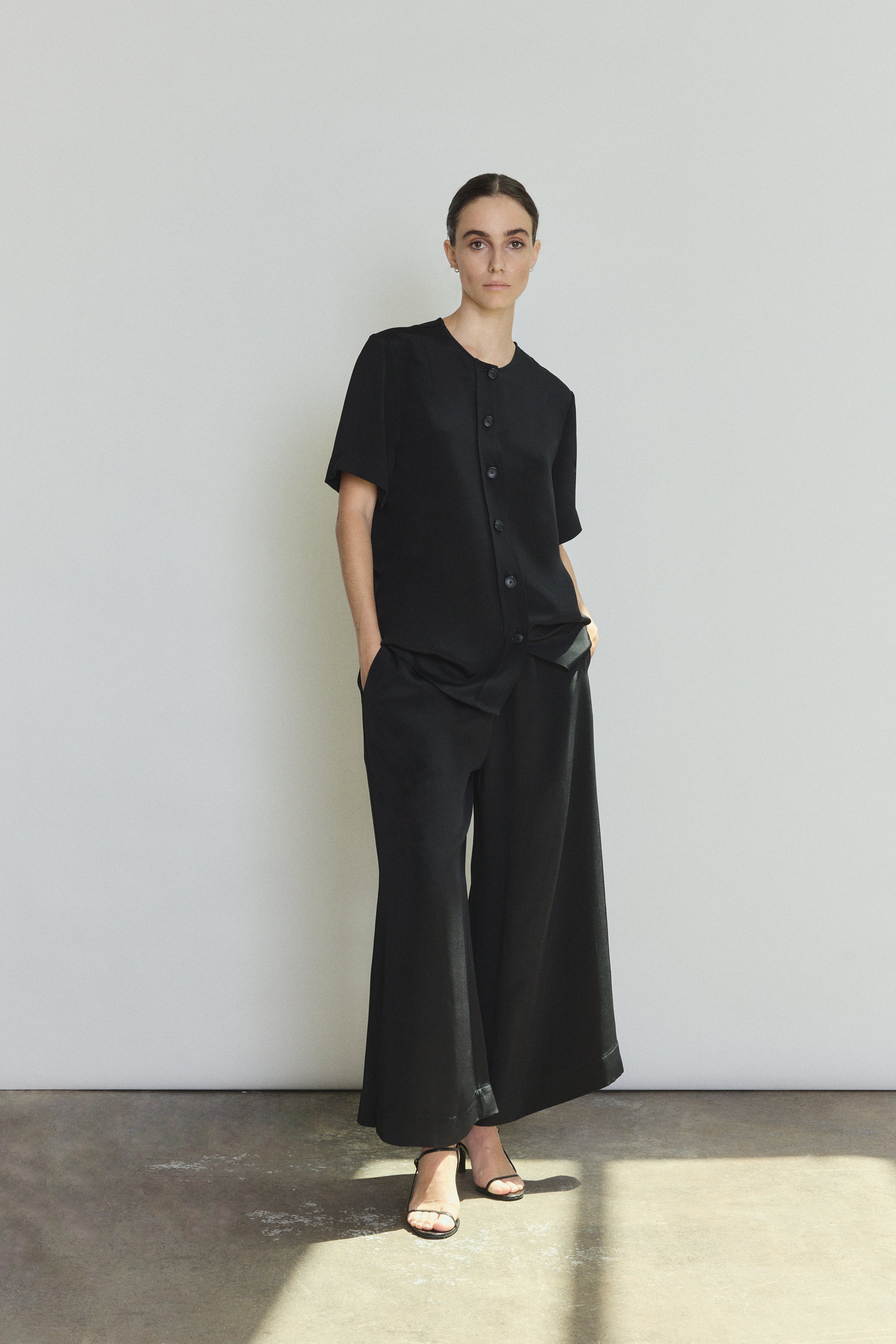 Front view of a model wearing the black silk crepe Kamperett Jette Silk Crepe Tee, an oversized reversible tee with wide button placket.