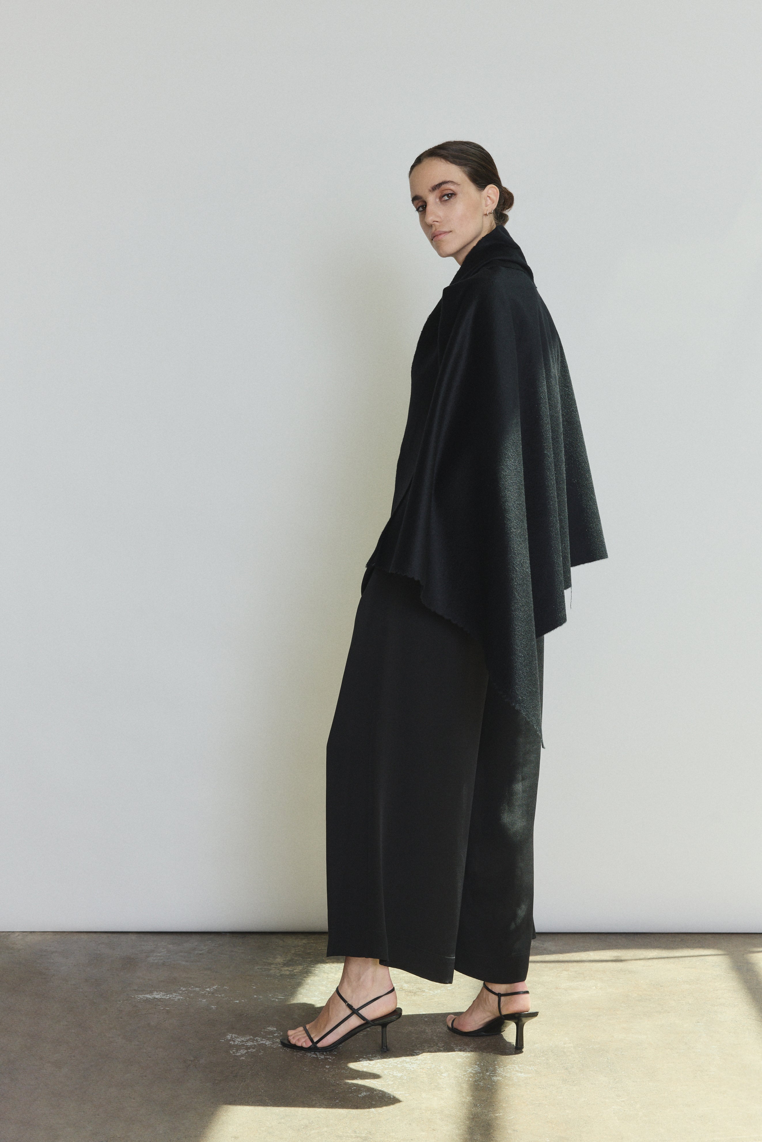 Back view of the black cashmere Kamperett Joan Cape showing the selvedge edges and full silhouette.