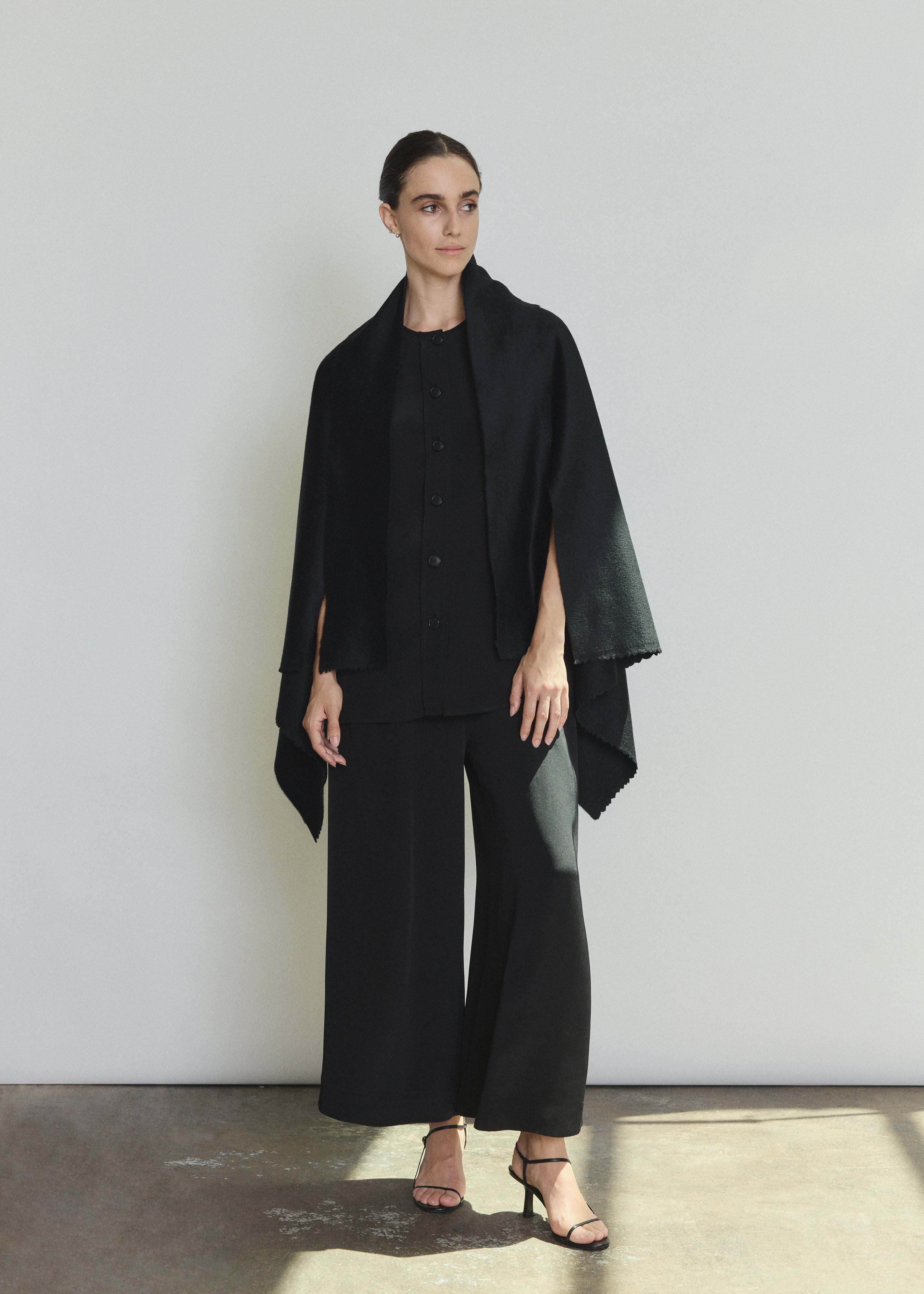 Side view of the black cashmere Kamperett Joan Cape showing the darted shoulder construction and attached scarf.