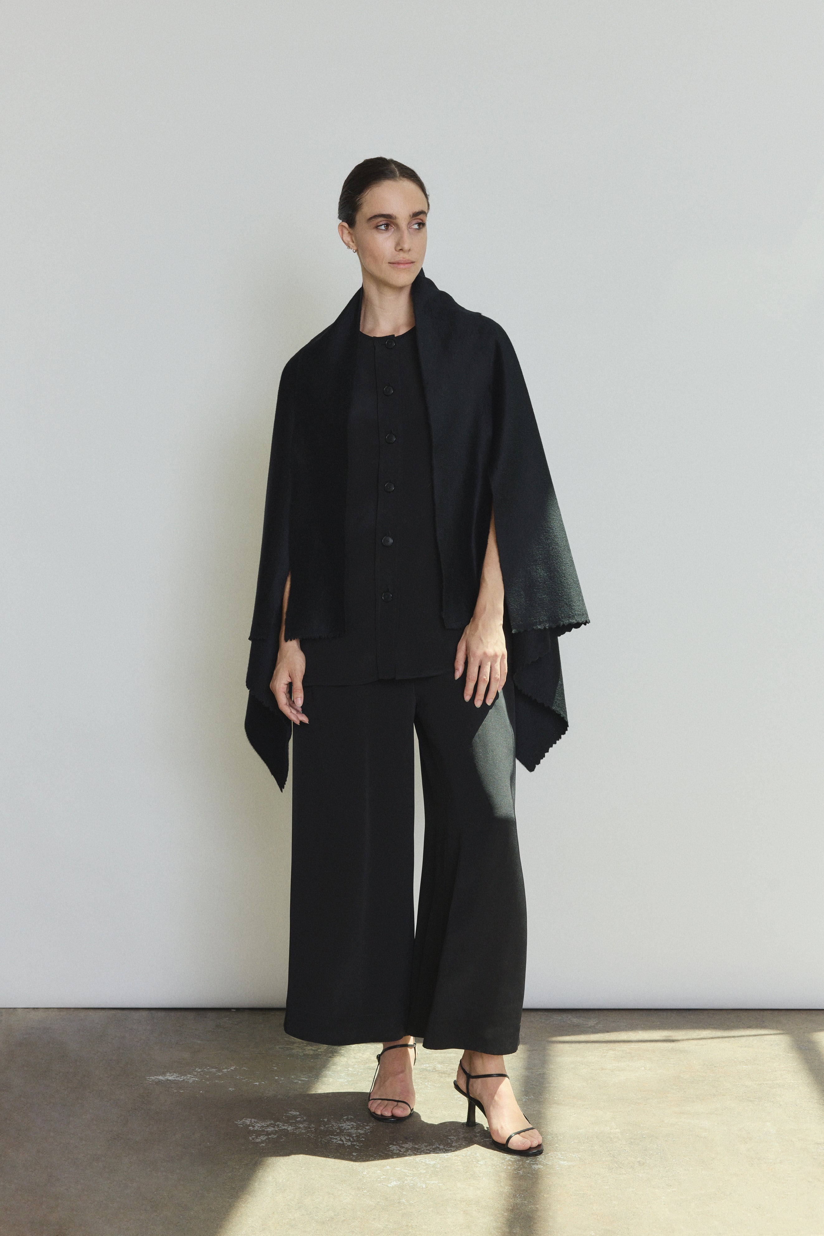 Side view of the black cashmere Kamperett Joan Cape showing the darted shoulder construction and attached scarf.