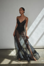Front view of a model wearing the black silk organza Kamperett Lalique Gown, a sheer V-neck maxi with multi-godet skirt and corded straps.
