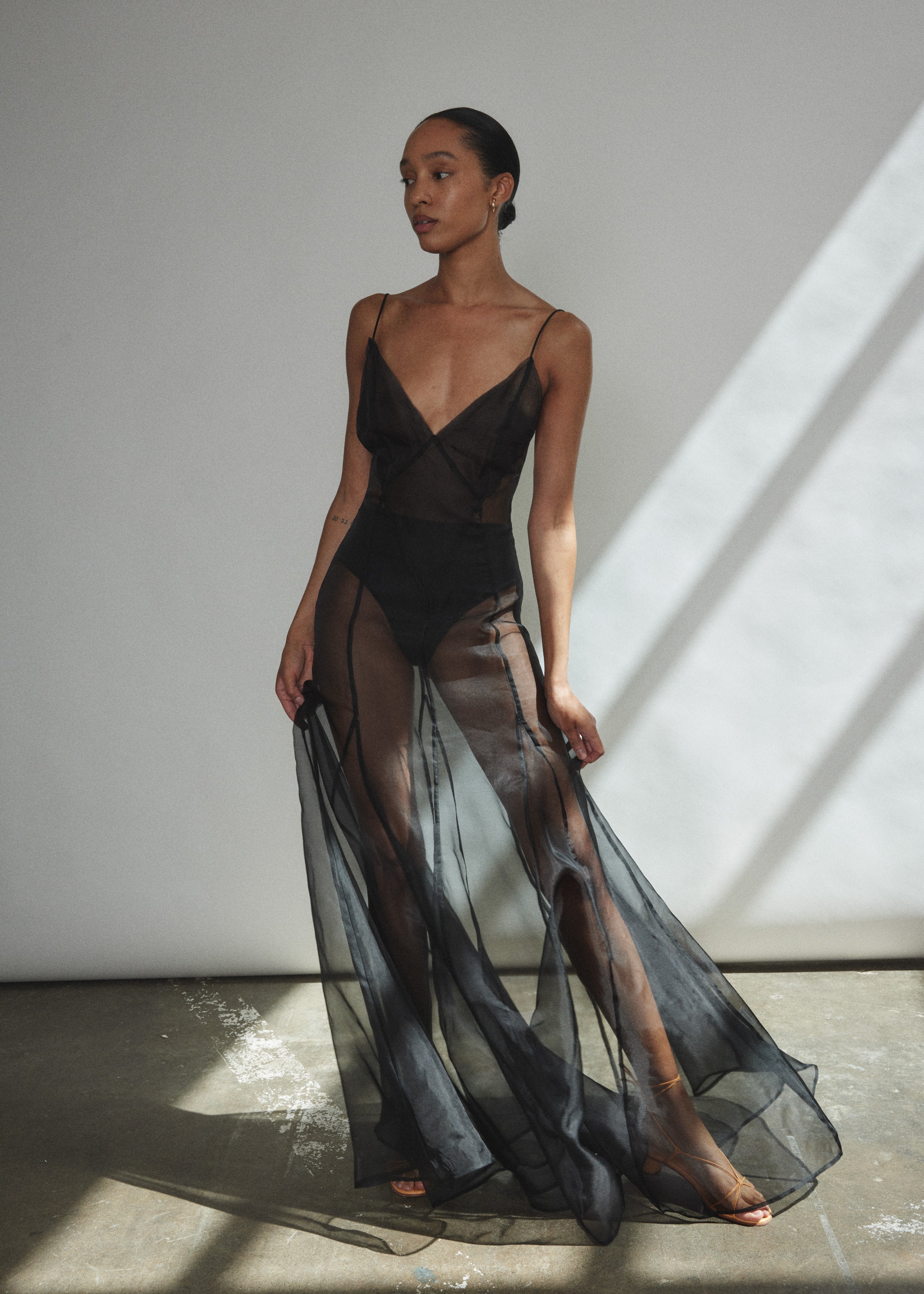 Front view of a model wearing the black silk organza Kamperett Lalique Gown, a sheer V-neck maxi with multi-godet skirt and corded straps.