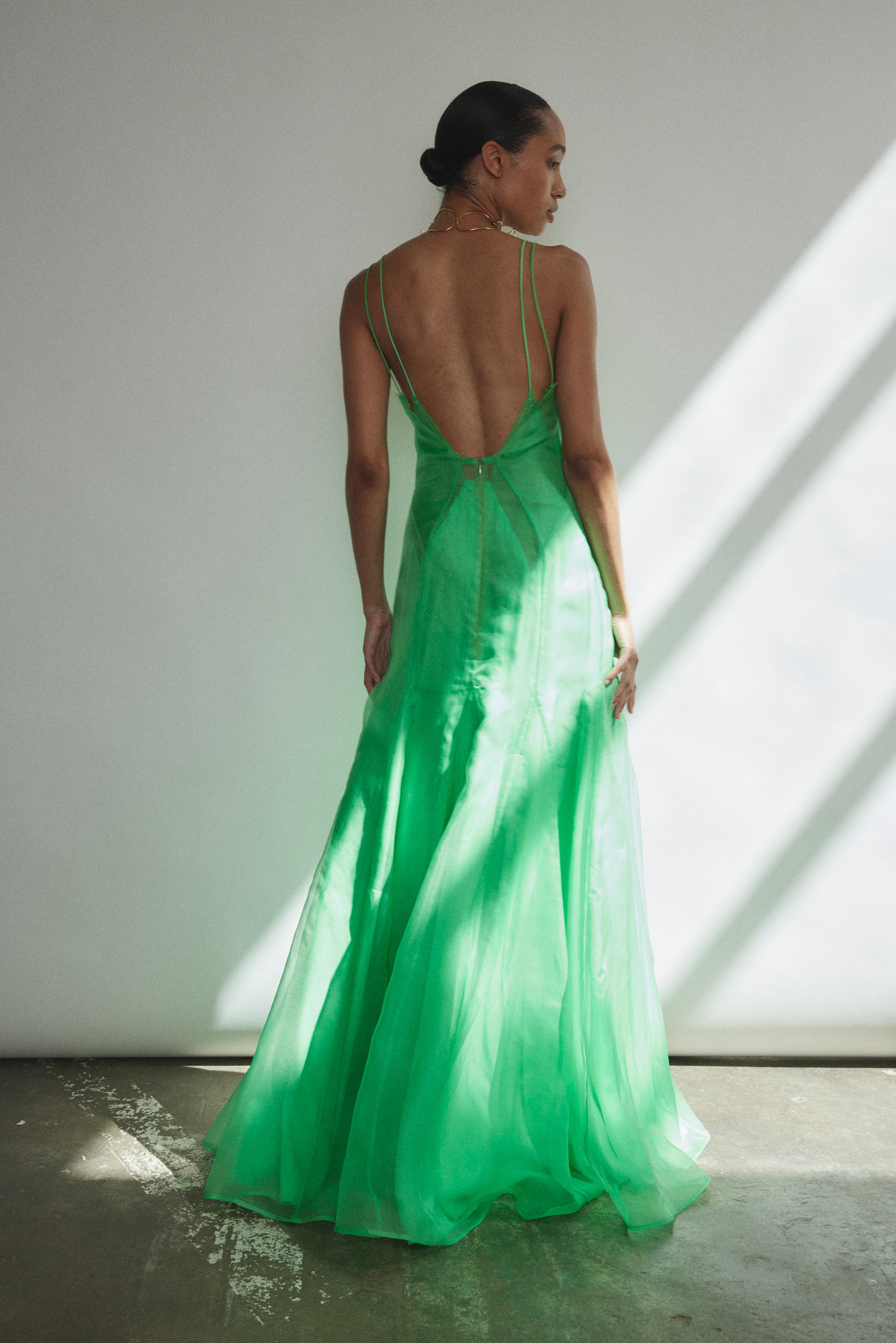 Front view of a model wearing the celadon silk organza Kamperett Lalique Gown, a sheer V-neck maxi with multi-godet skirt and corded straps.
