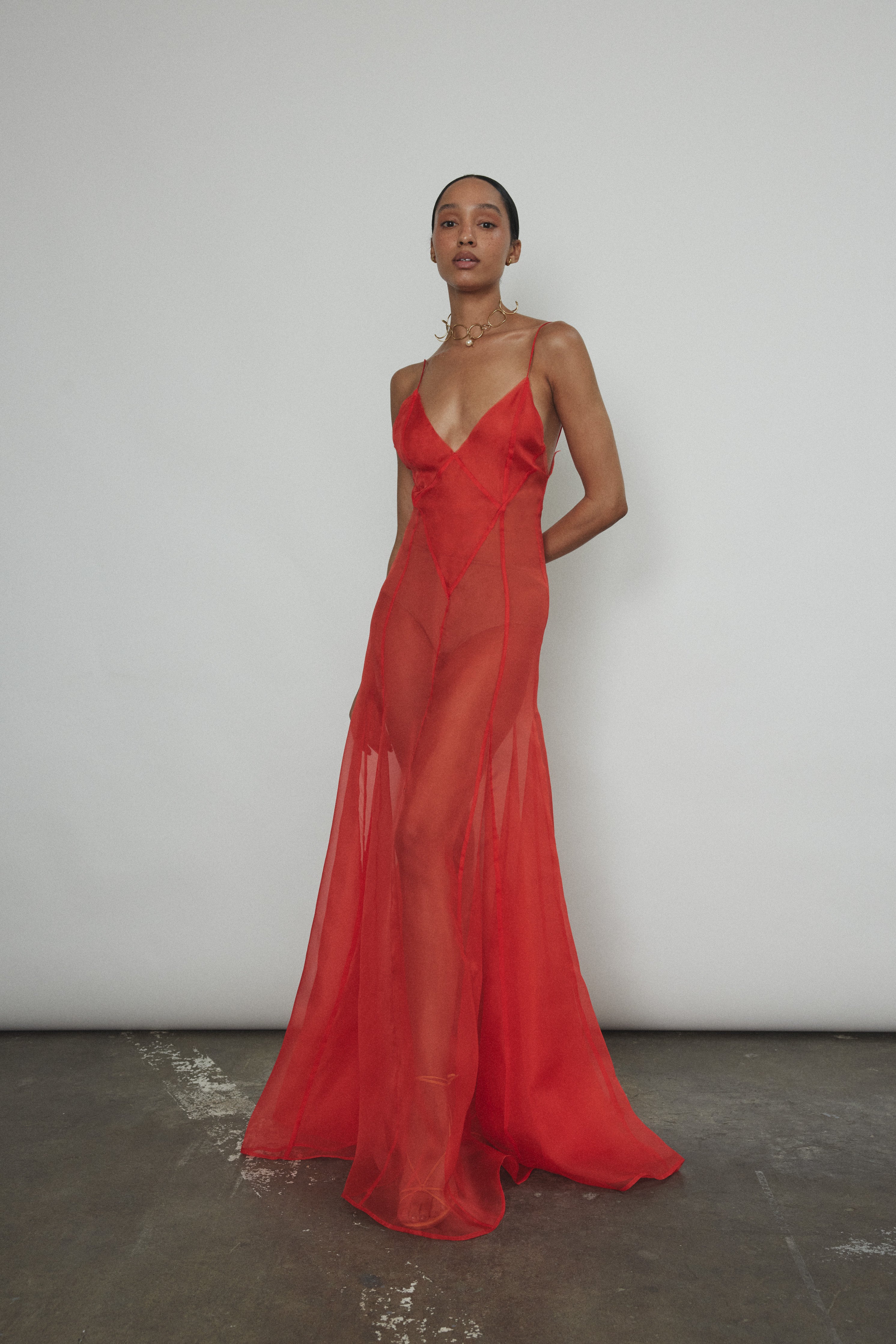Front view of a model wearing the vermilion silk organza Kamperett Lalique Gown, a sheer V-neck maxi with multi-godet skirt.