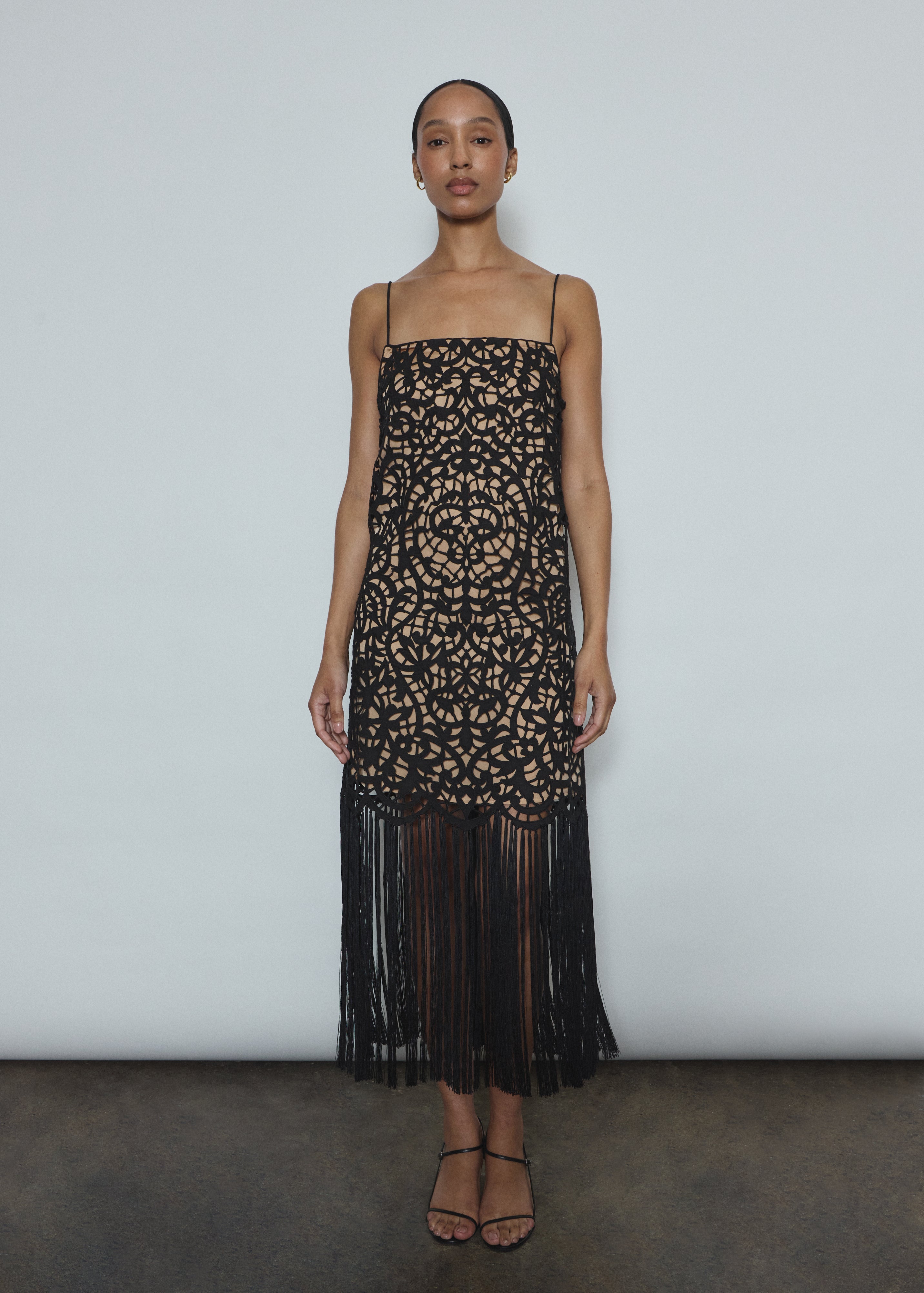 Front view of a model wearing the black cotton openwork Kamperett Lenore Dress, an A-line midi with square neckline, spaghetti straps, and hand-applied fringe.