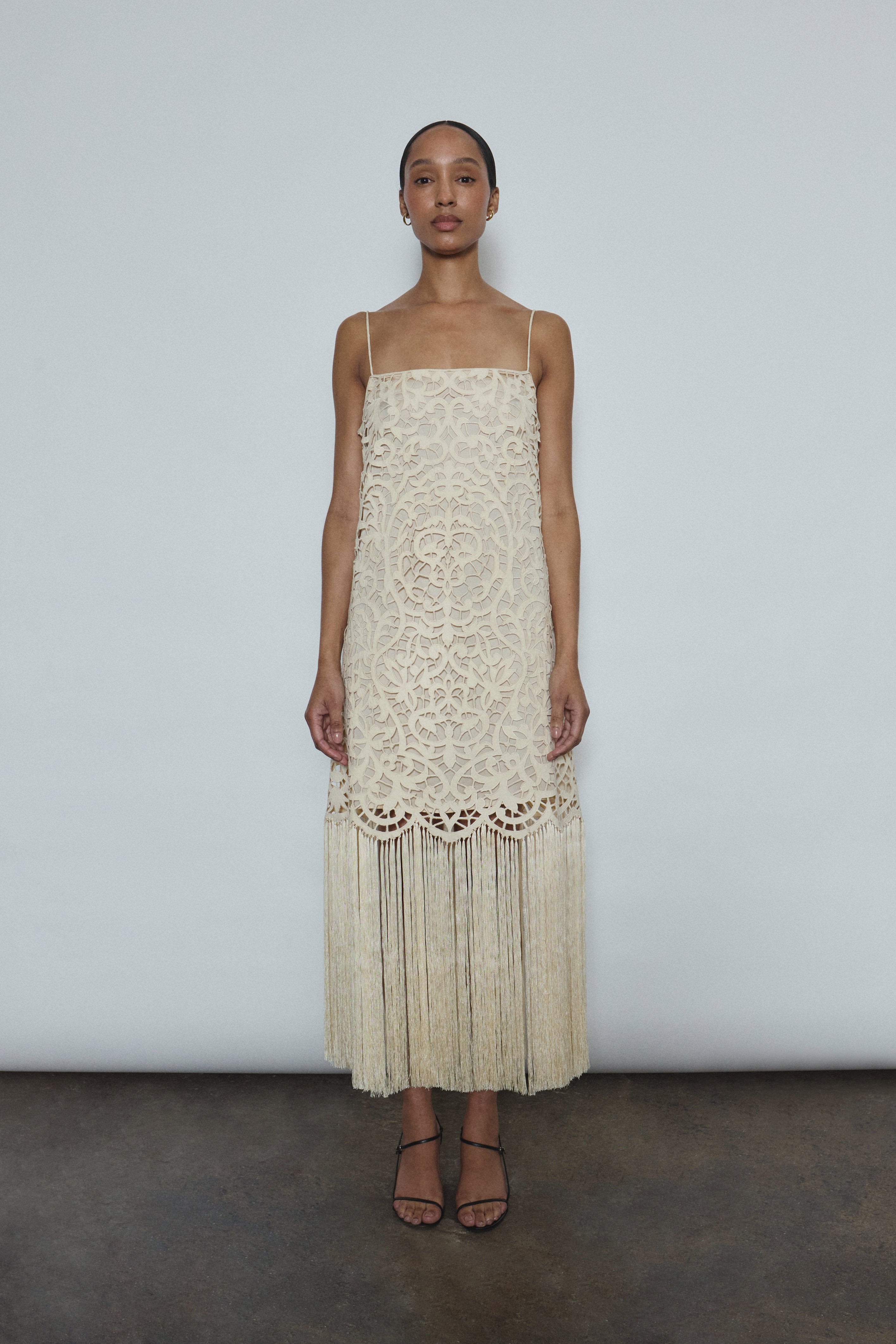 Front view of a bride wearing the cream cotton openwork Kamperett Lenore Dress, an A-line midi with square neckline, spaghetti straps, and hand-applied fringe.