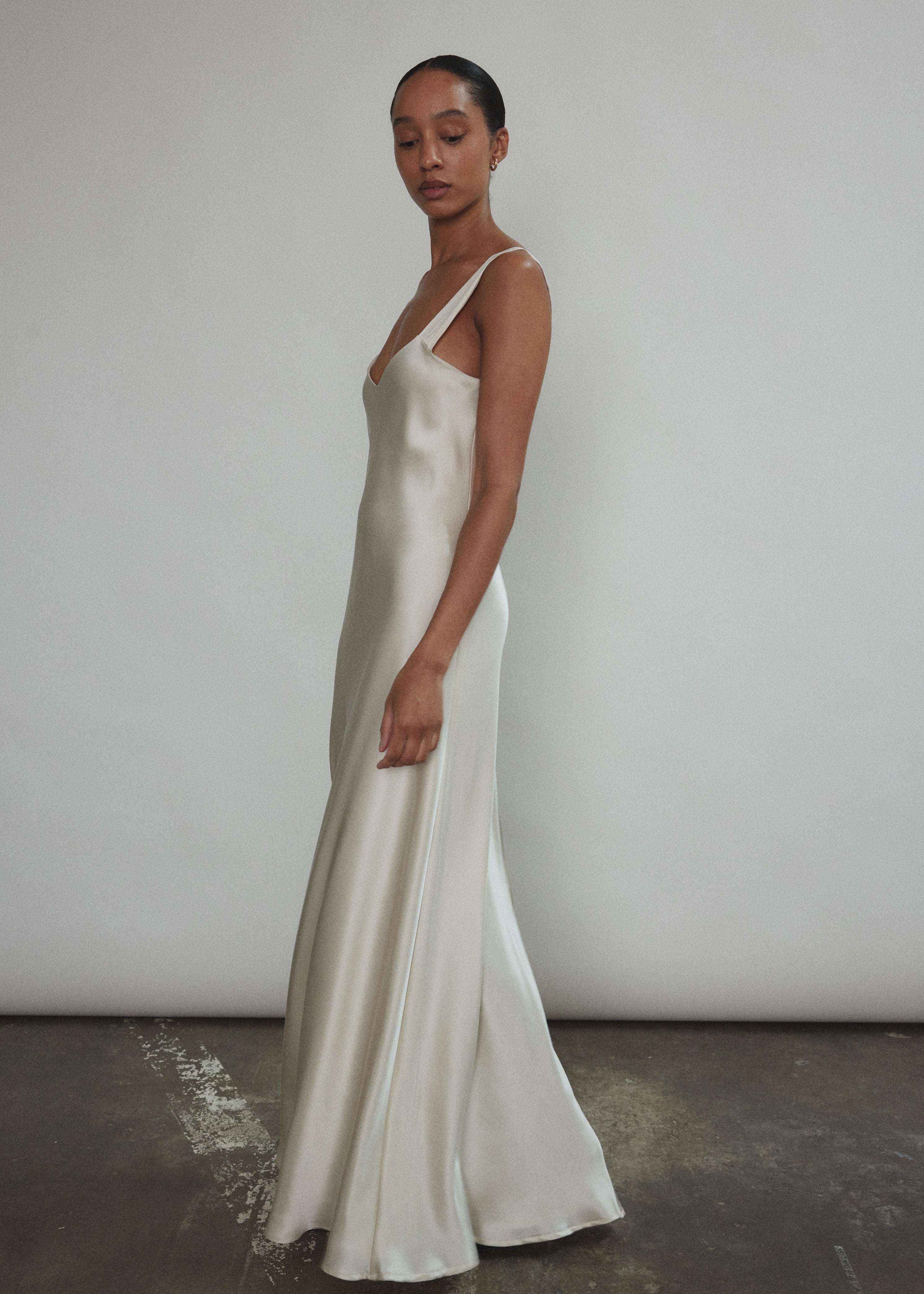 Angled view of the ivory silk charmeuse Kamperett Lisette Maxi Slip Dress, showing the bias-cut drape and maxi length.