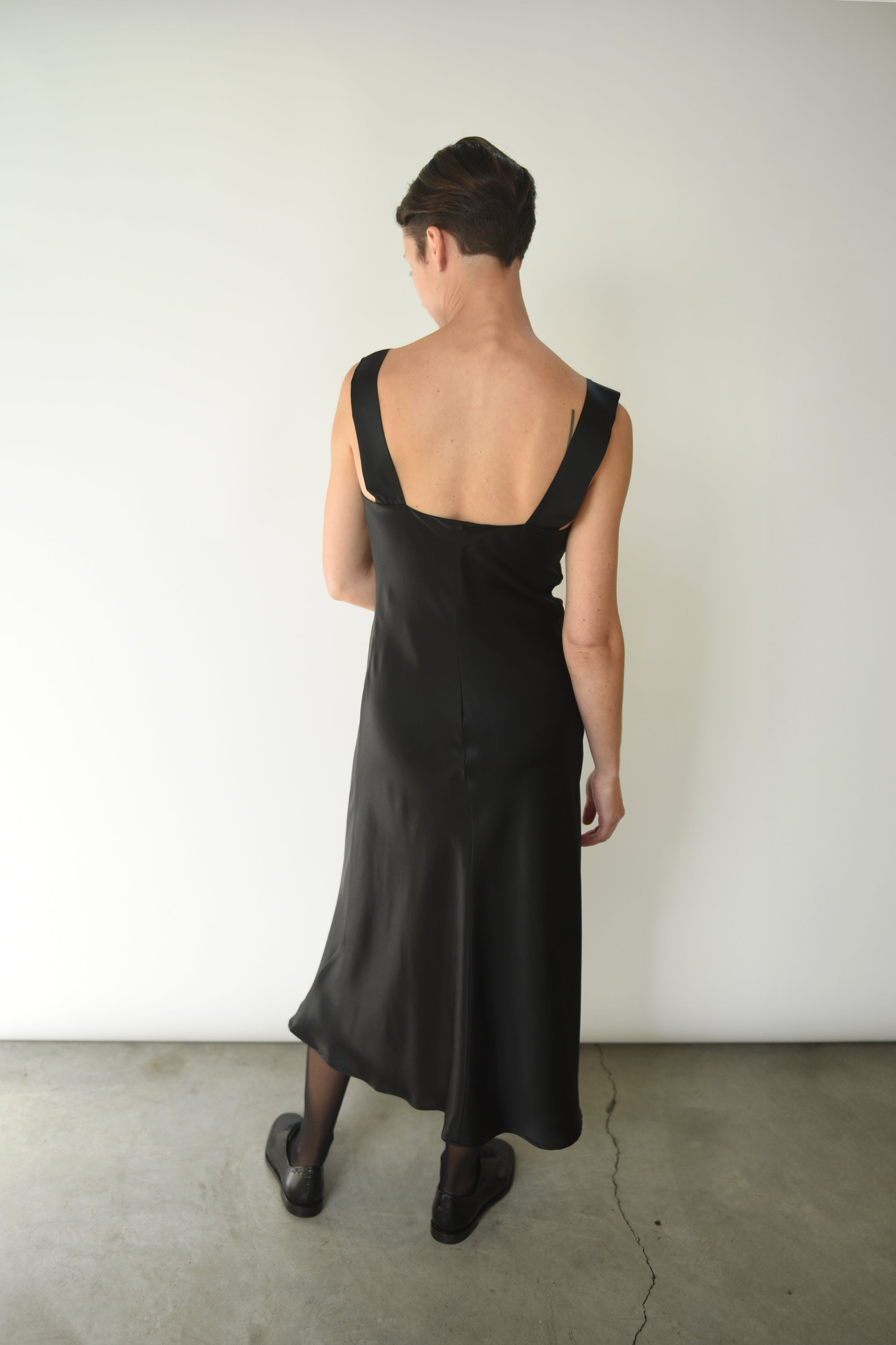 Back view of the black silk charmeuse Kamperett Lisette Midi Slip Dress with straight-cut back and wider straps.