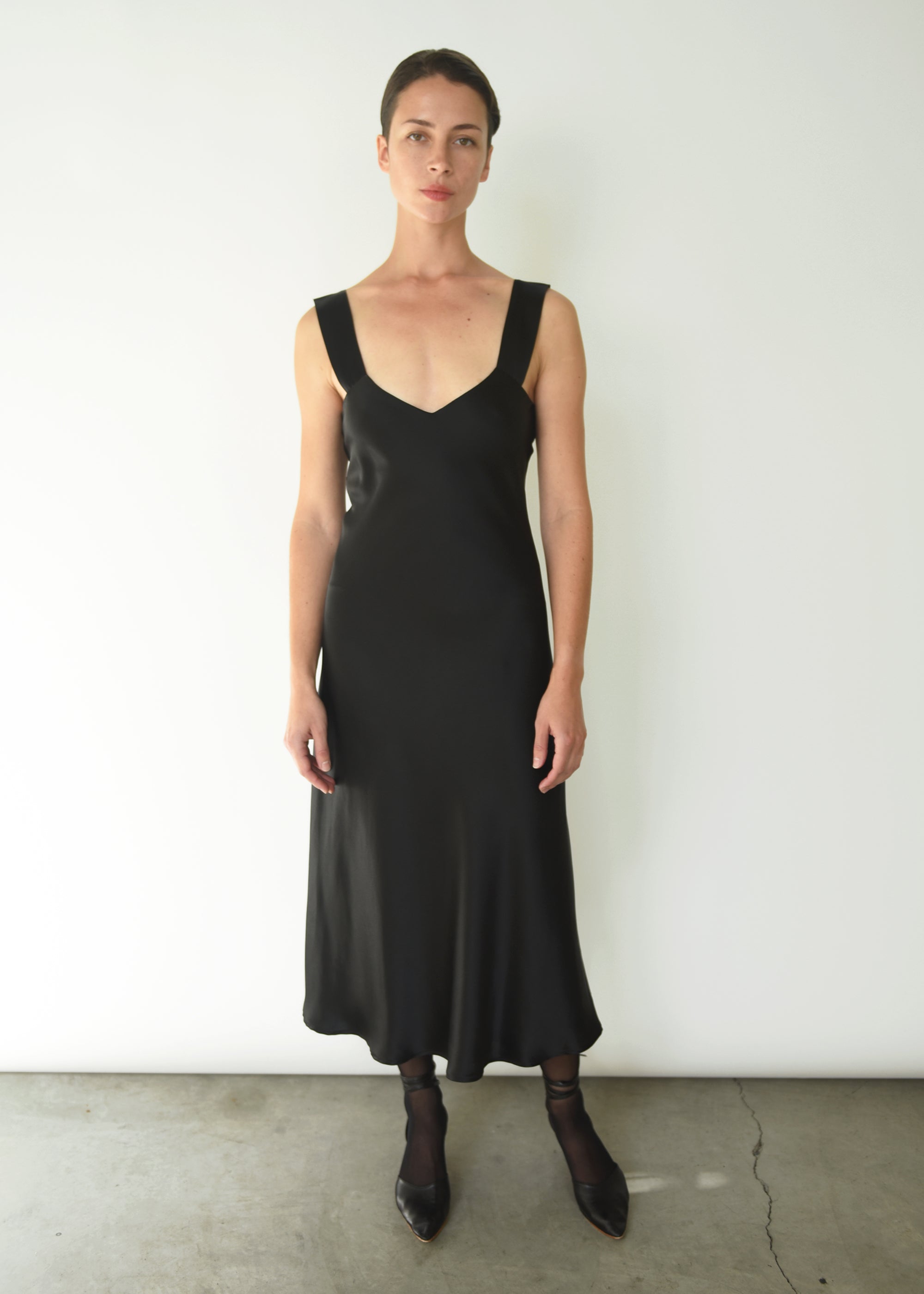 Front view of a model wearing the black silk charmeuse Kamperett Lisette Midi Slip Dress with V-neck and wider straps.