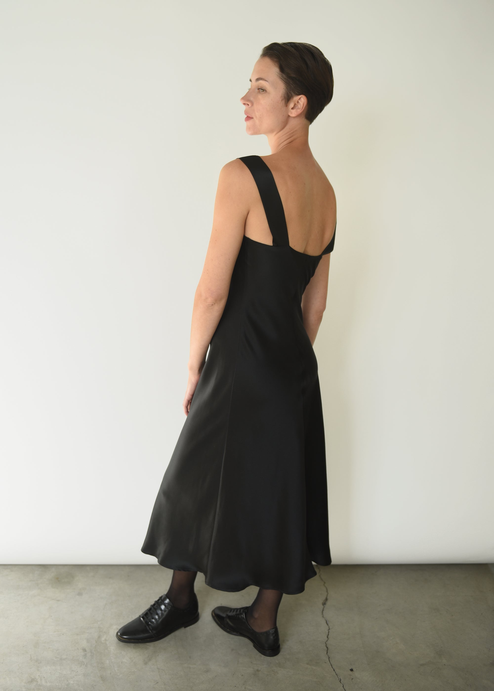 Side view of the black silk charmeuse Kamperett Lisette Midi Slip Dress, showing the bias-cut drape.