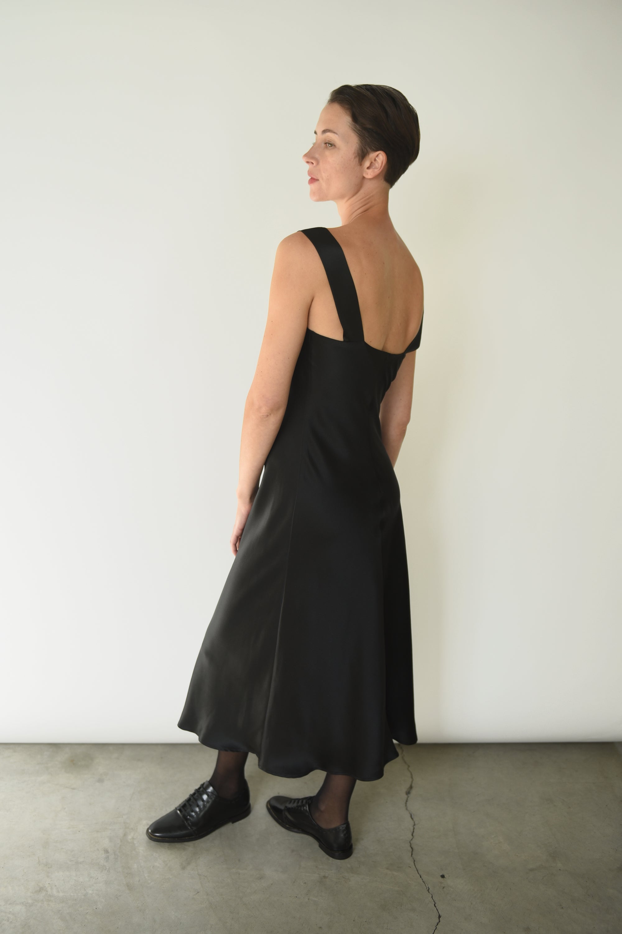 Side view of the black silk charmeuse Kamperett Lisette Midi Slip Dress, showing the bias-cut drape.