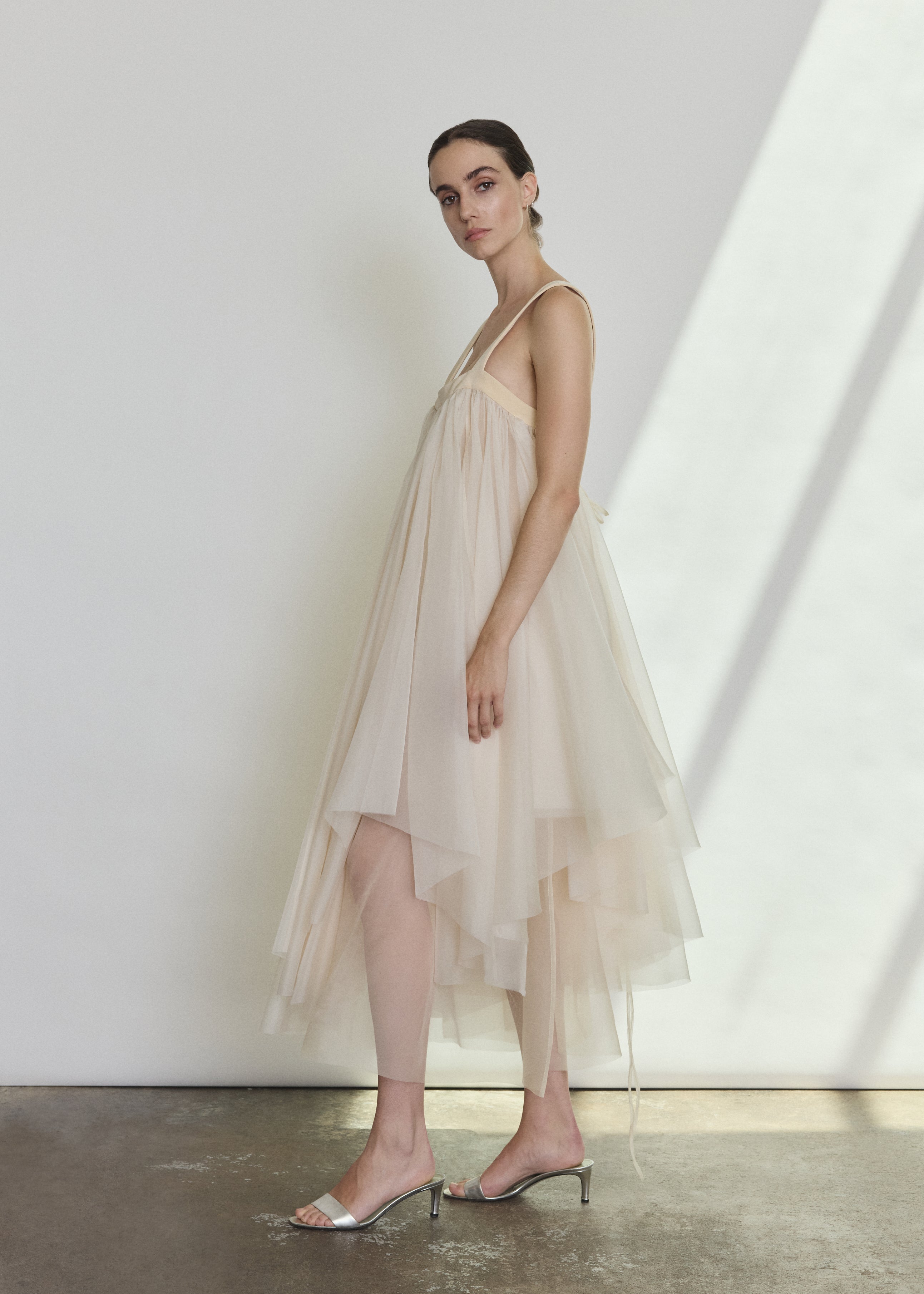 Side view of the ivory silk organza Kamperett Loie Dress showing the asymmetrical tiered silhouette and silk cord waist tie.
