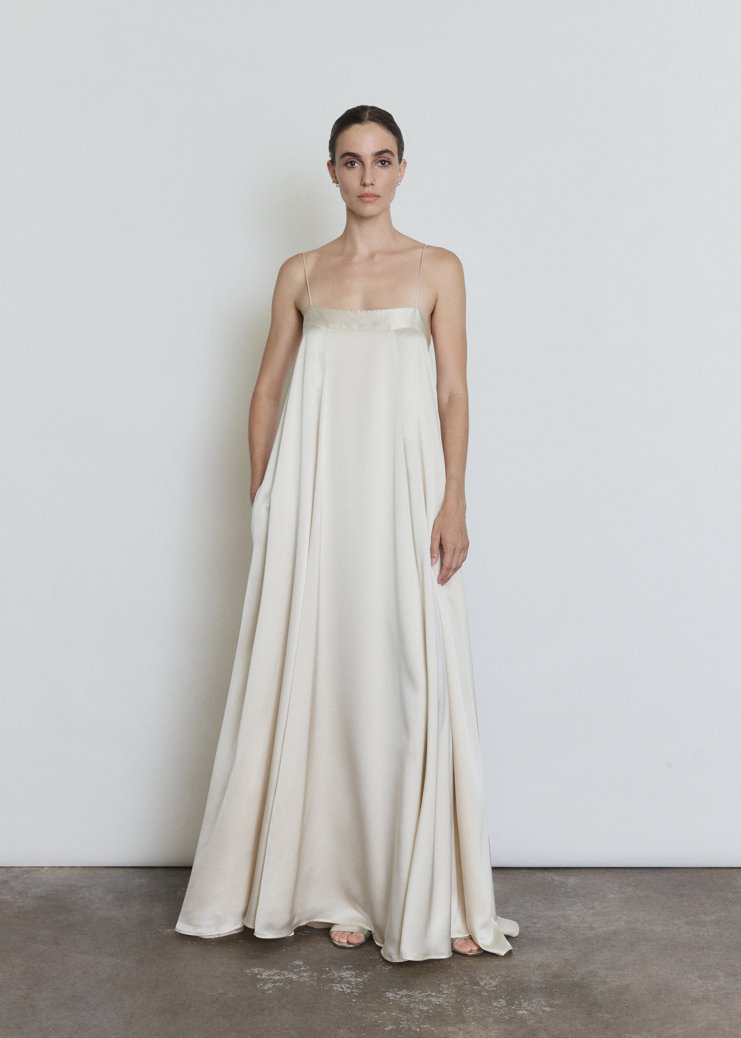 Front view of a bride wearing the ivory silk Kamperett Metronome Gown, a sleek column wedding gown with sweeping hem and corded straps.