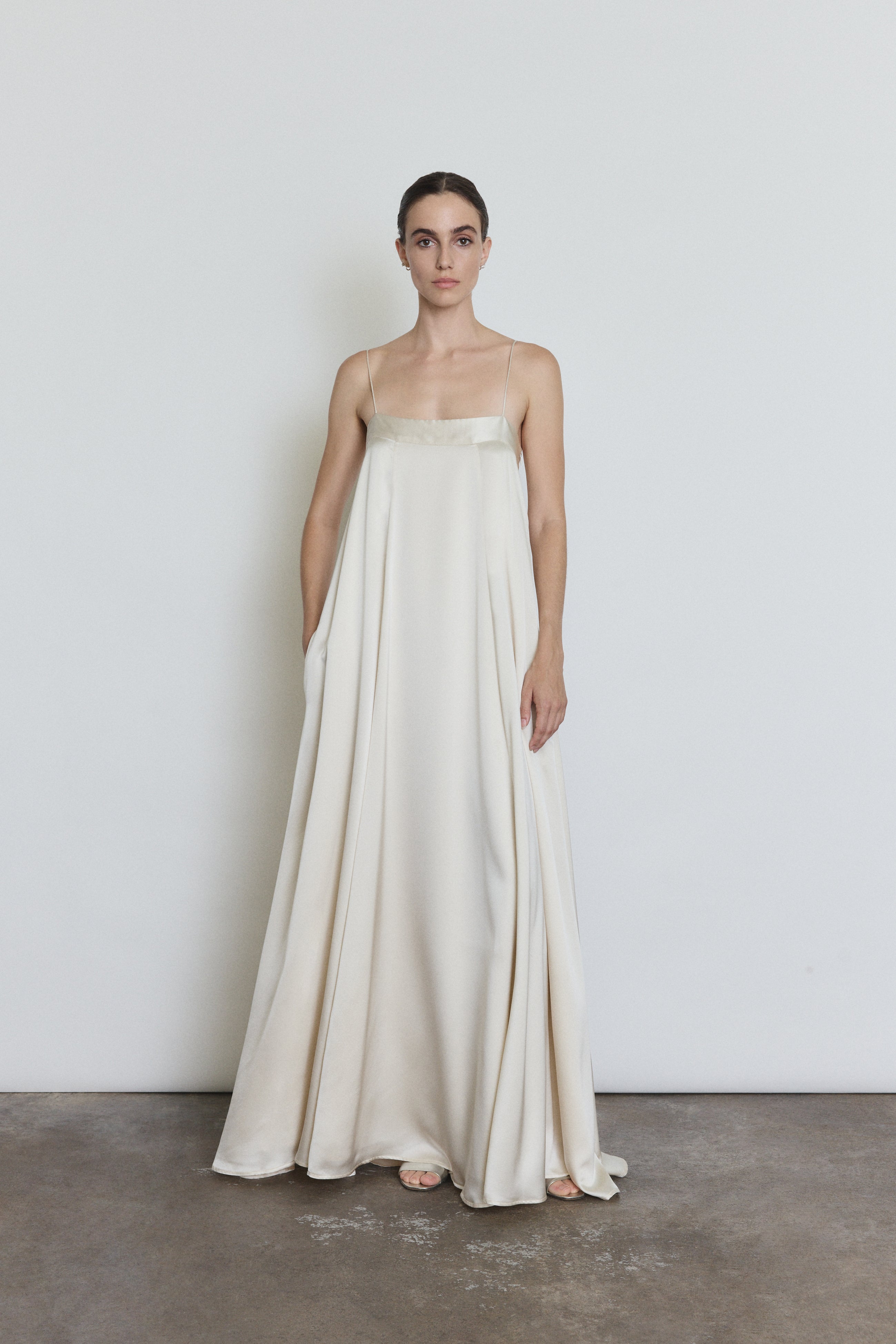 Front view of a bride wearing the ivory silk Kamperett Metronome Gown, a sleek column wedding gown with sweeping hem and corded straps.