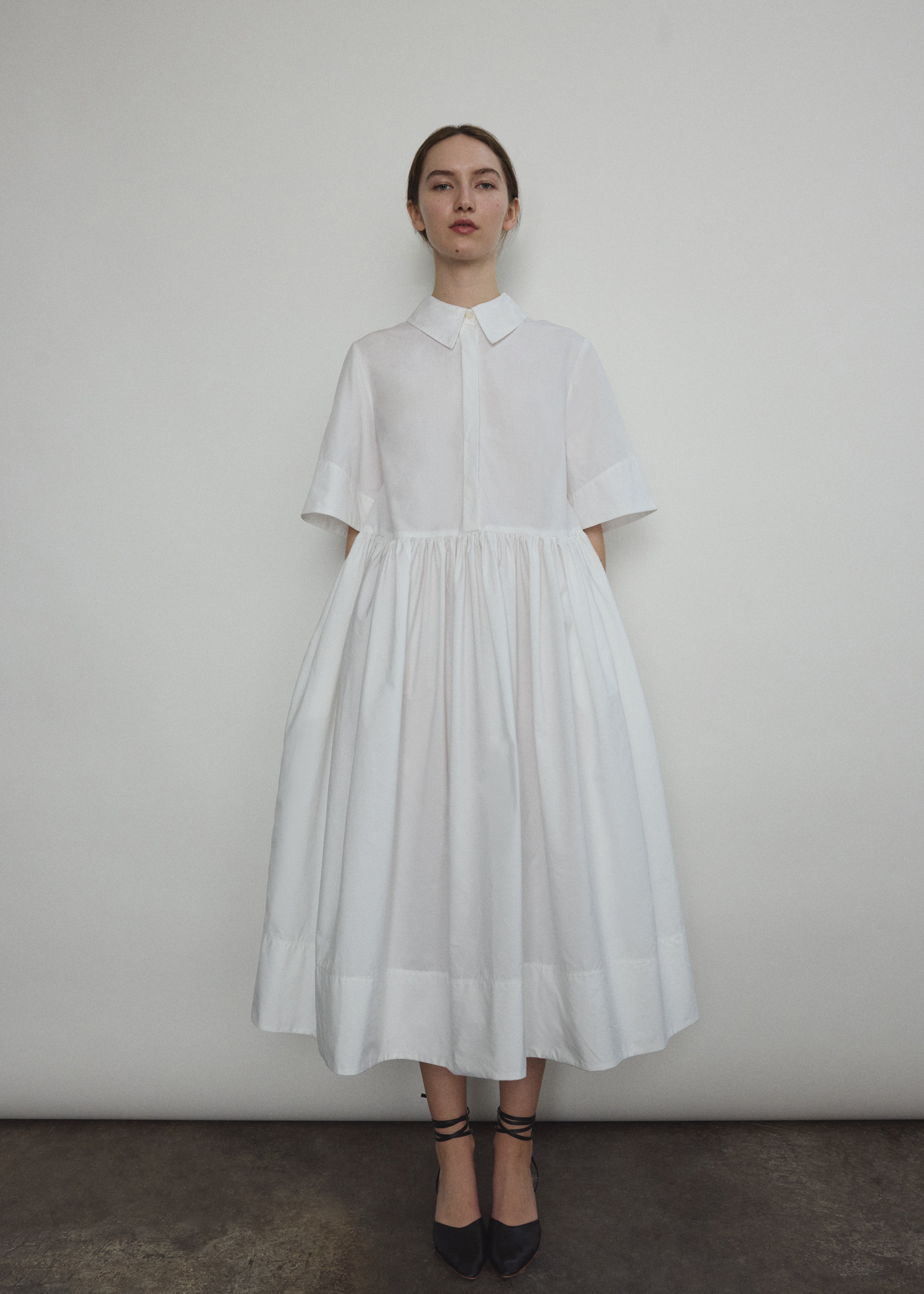 Front view of a model wearing the white Japanese cotton lawn Kamperett Miller Dress, an oversized shirt dress with button front.