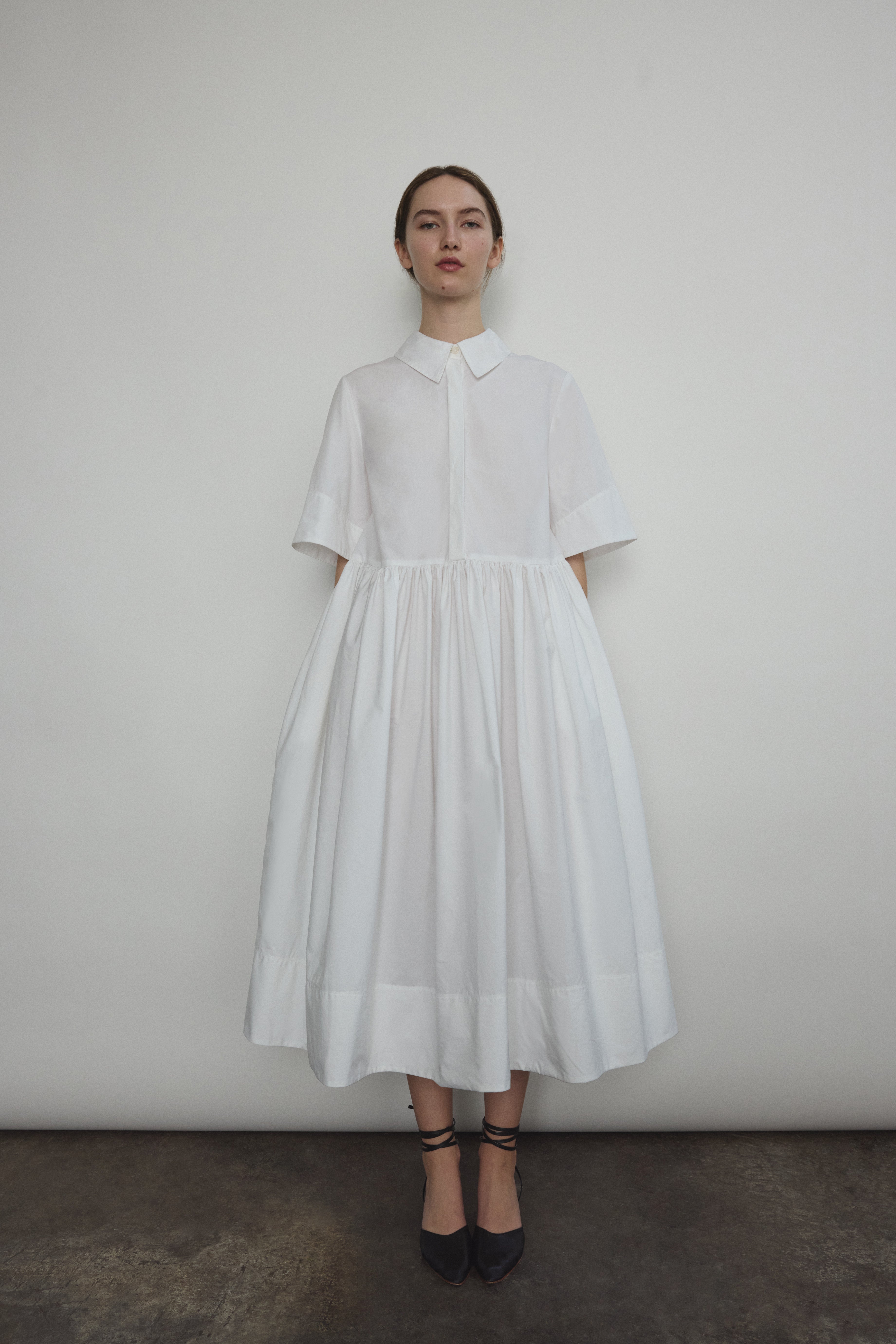 Front view of a model wearing the white Japanese cotton lawn Kamperett Miller Dress, an oversized shirt dress with button front.