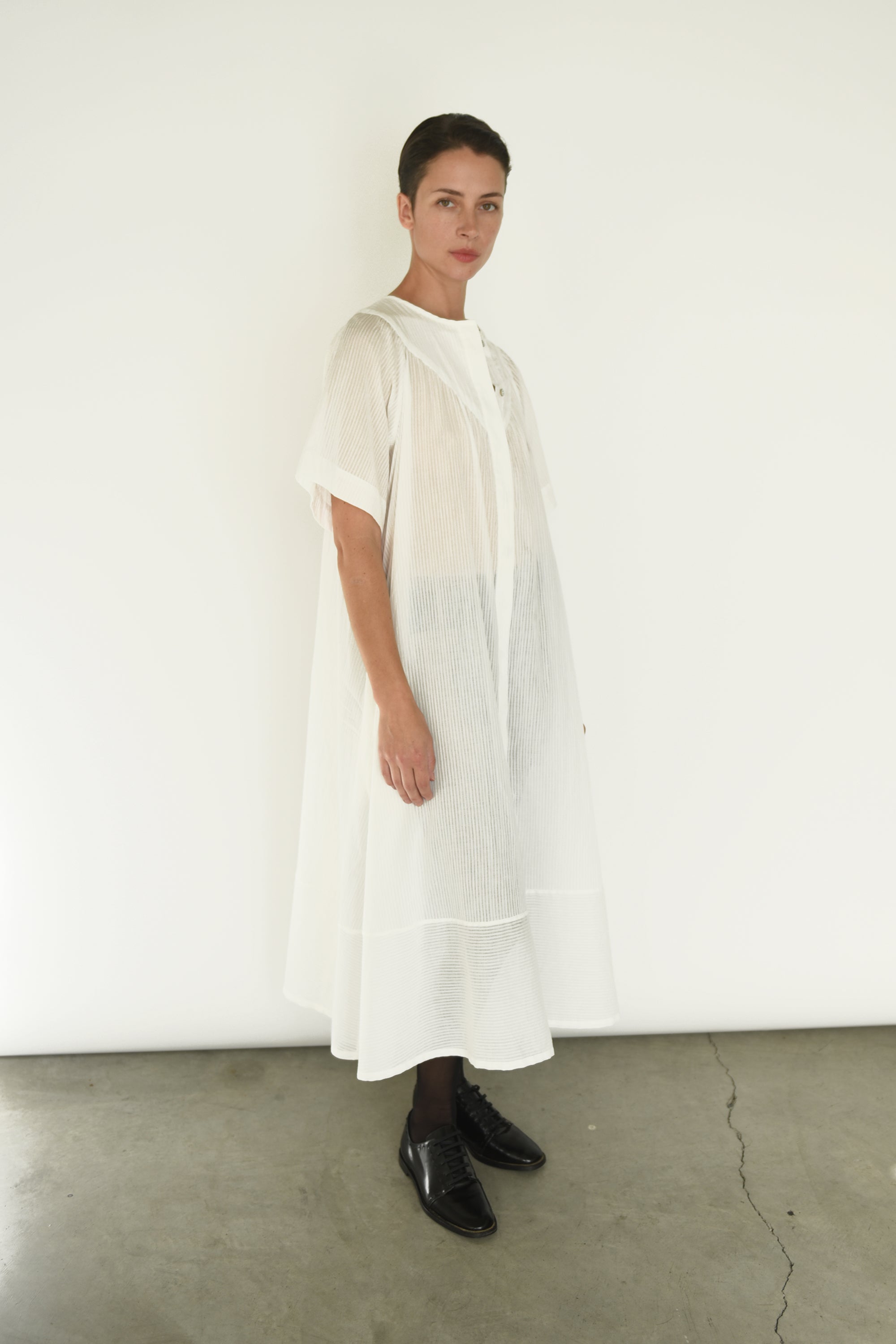 Angled view of the white Japanese cotton voile Kamperett Oma Dress with hidden placket button front.