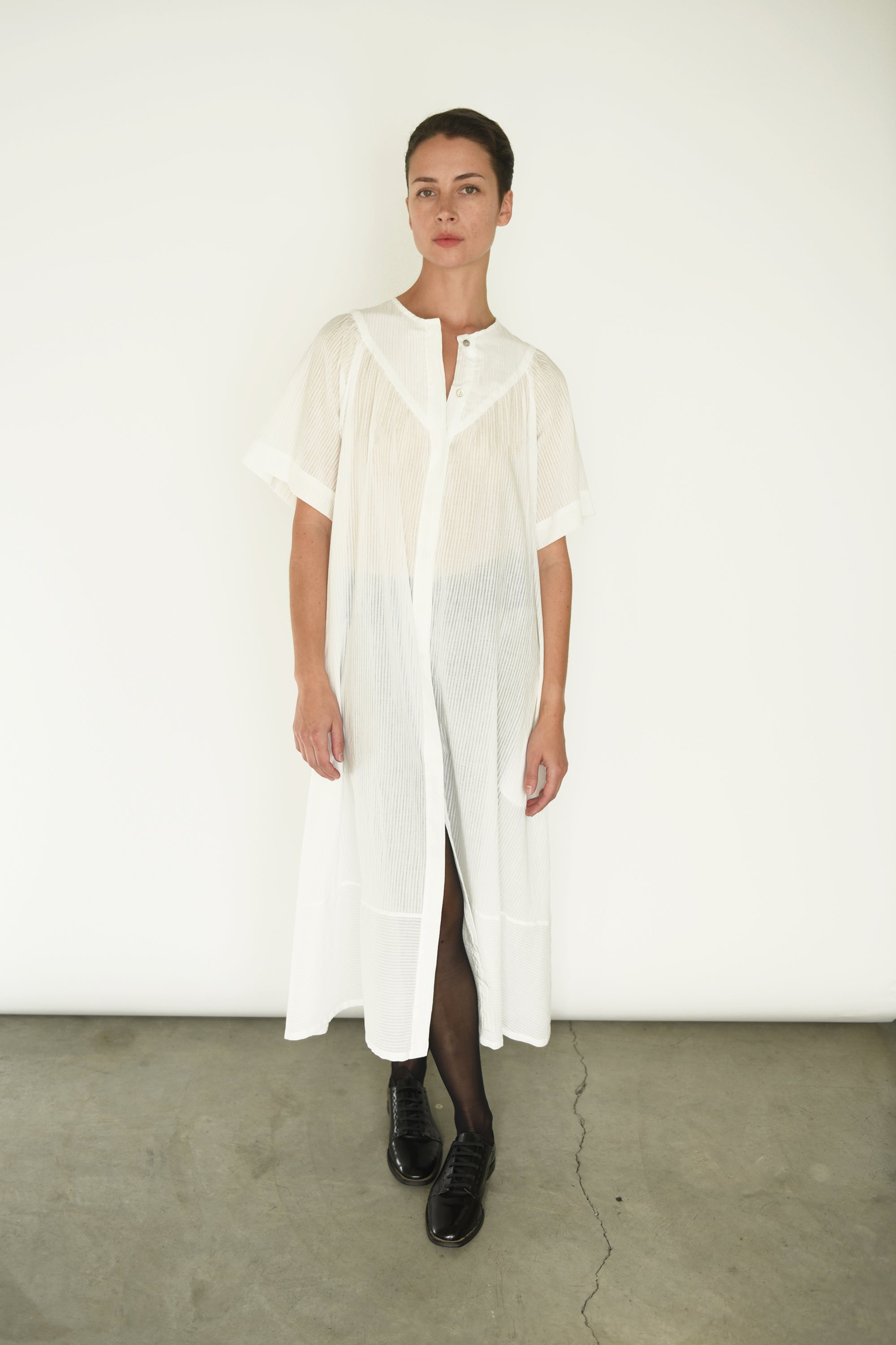 Front view of a model wearing the white semi-sheer Japanese cotton voile Kamperett Oma Dress, with gathered yoke and dolman sleeves.