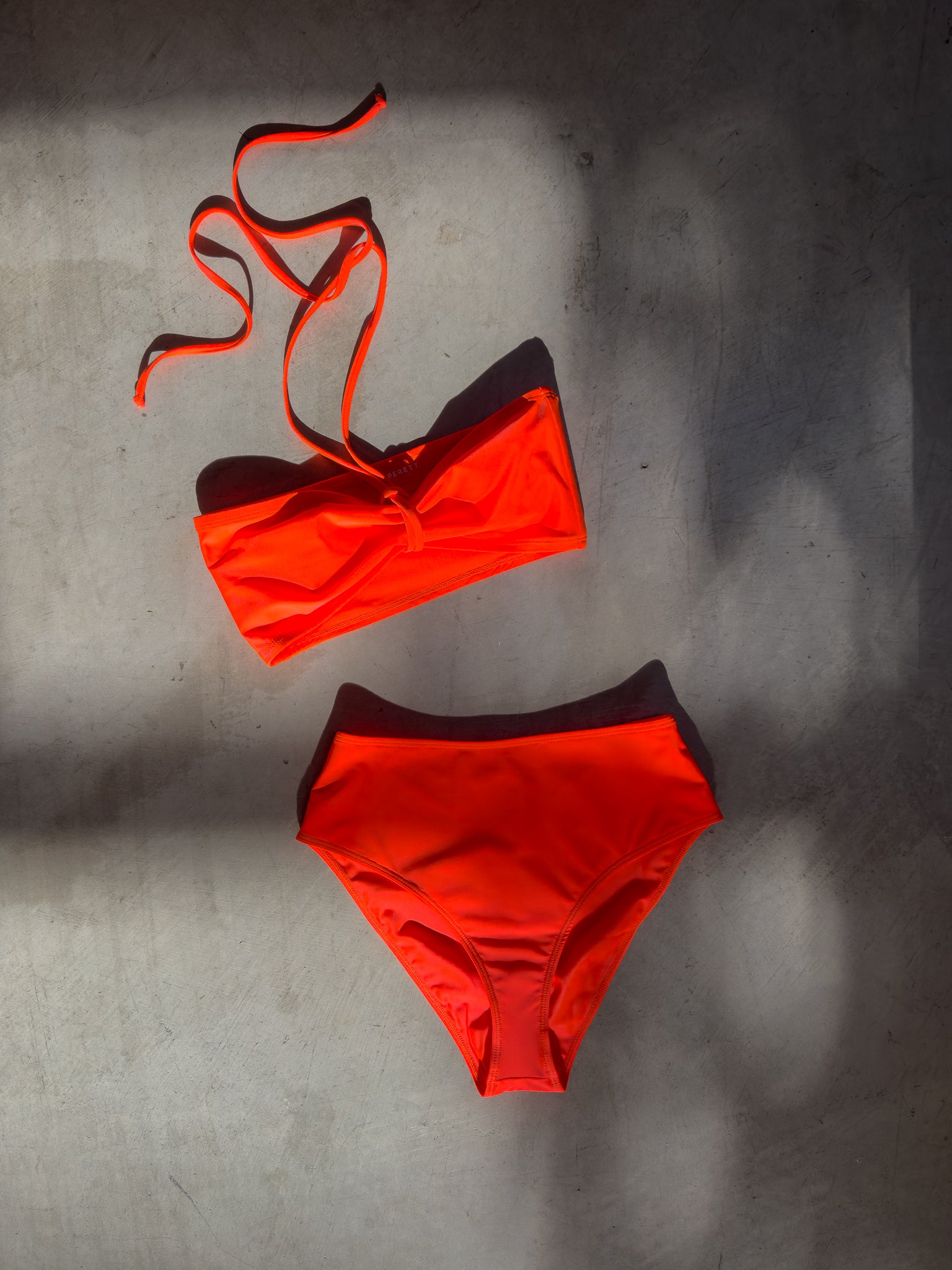 Editorial image of a model in the coral Italian regenerated nylon Kamperett Orra swim set (Bandeau Top and High Waist Brief).