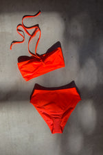 Editorial image of a model in the coral Italian regenerated nylon Kamperett Orra swim set (Bandeau Top and High Waist Brief).