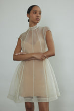 Front view of a bride wearing the ivory silk organza Kamperett Reine Dress, an intricately seamed mini with mock neck.