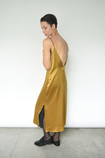 Angled view of the brass silk charmeuse Kamperett Sade Slip Dress.