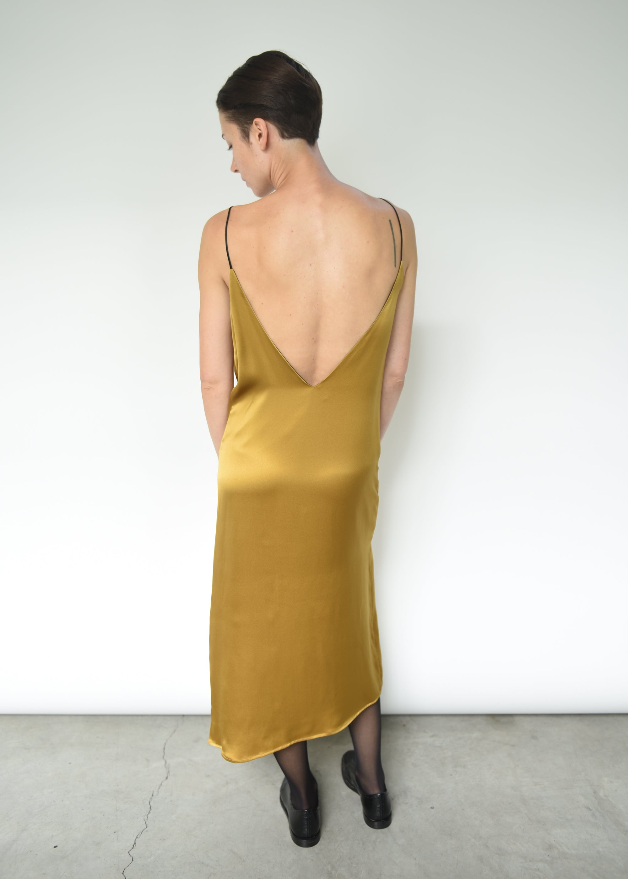 Back-angled view of the brass silk charmeuse Kamperett Sade Slip Dress.
