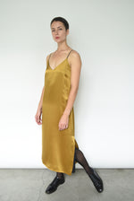 Front view of a model wearing the brass silk charmeuse Kamperett Sade Slip Dress, a straight-cut midi with corded straps.