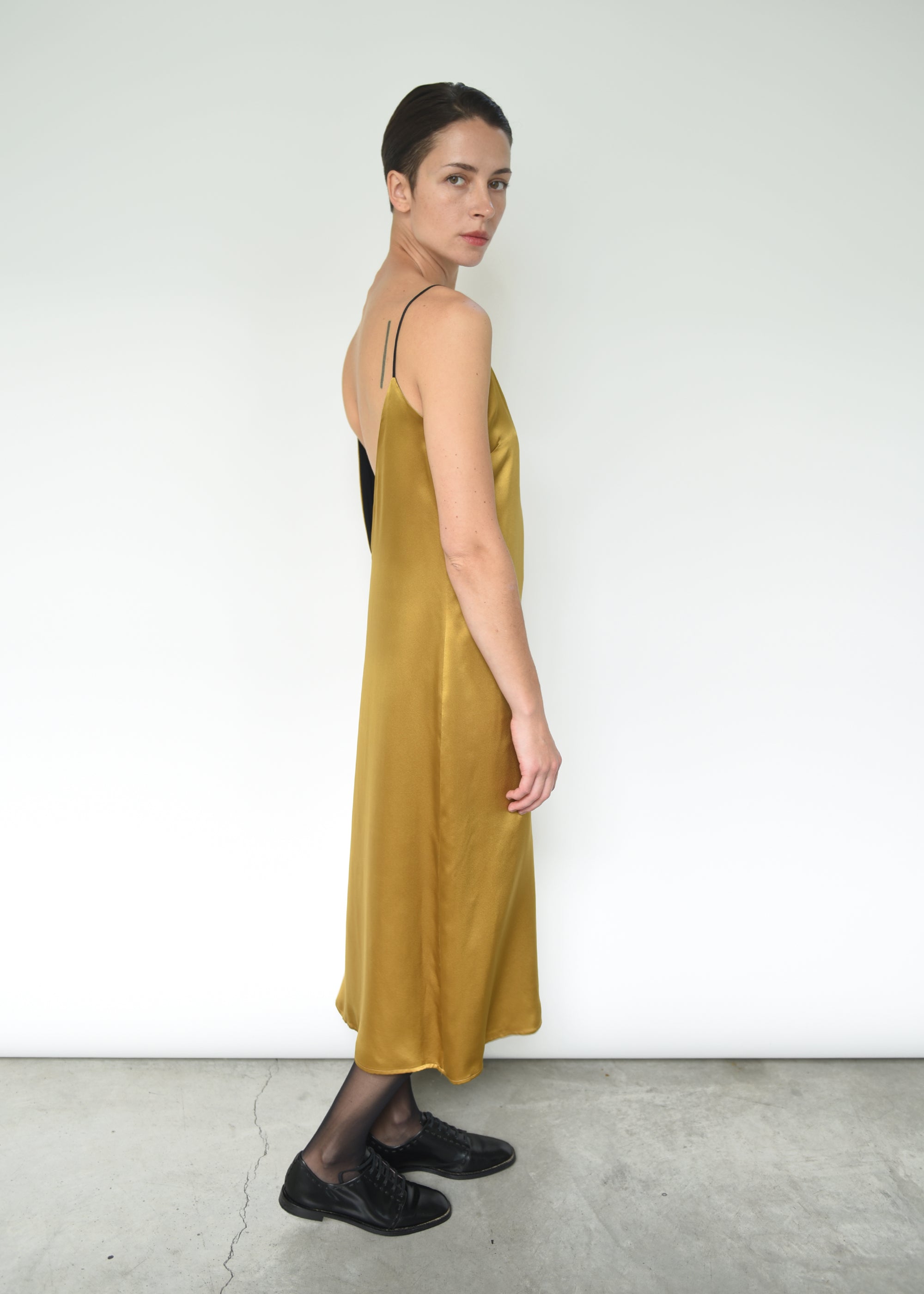 Side view of the brass silk charmeuse Kamperett Sade Slip Dress, showing the loose silhouette.