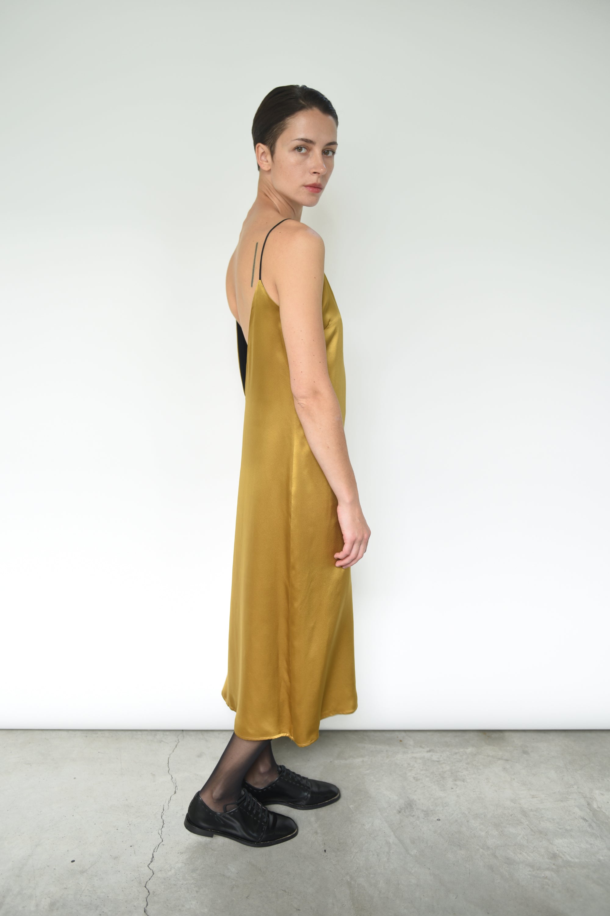 Side view of the brass silk charmeuse Kamperett Sade Slip Dress, showing the loose silhouette.