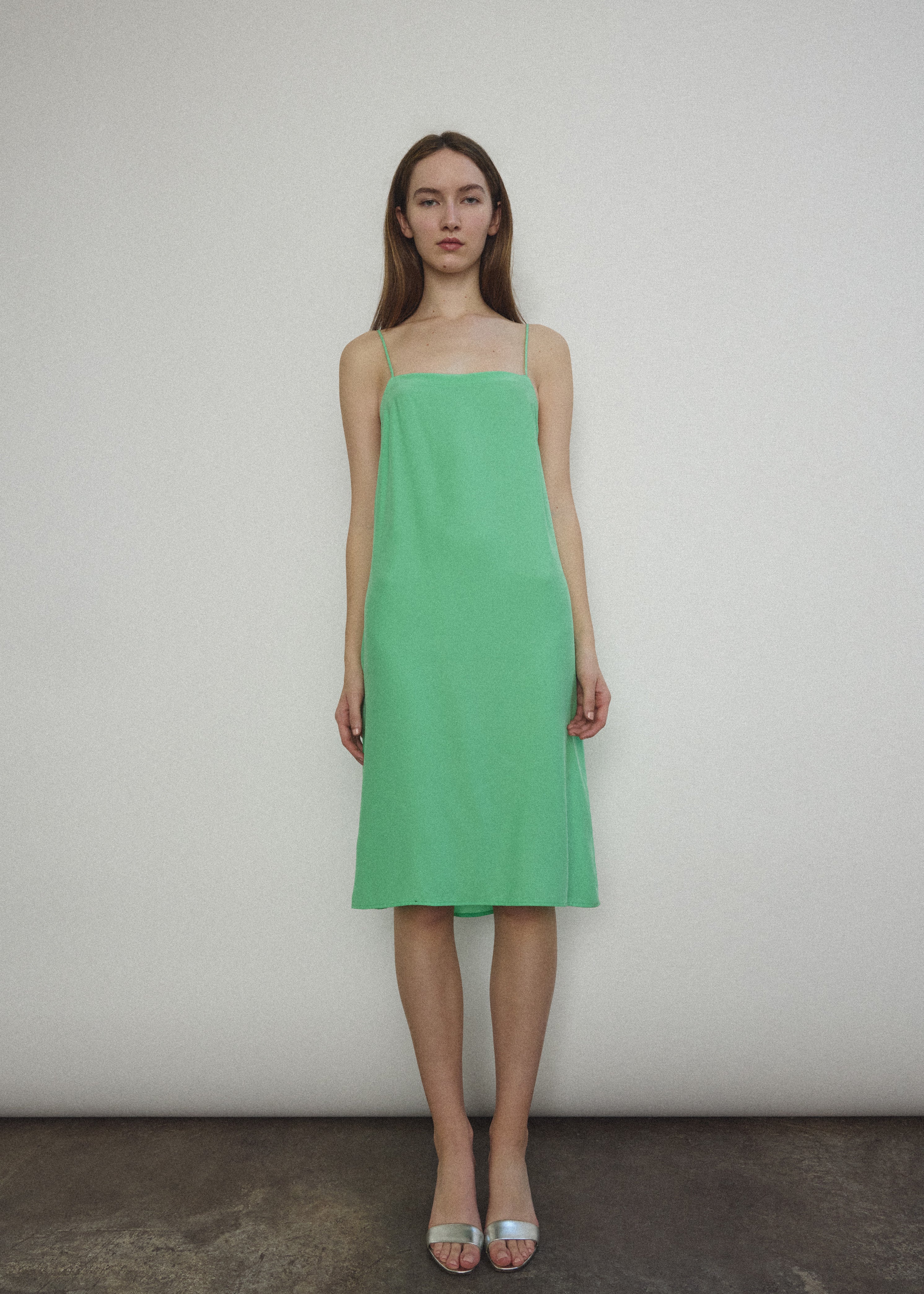 Front view of a model wearing the celadon silk charmeuse Kamperett Short Slip, a midi slip with fixed spaghetti straps.