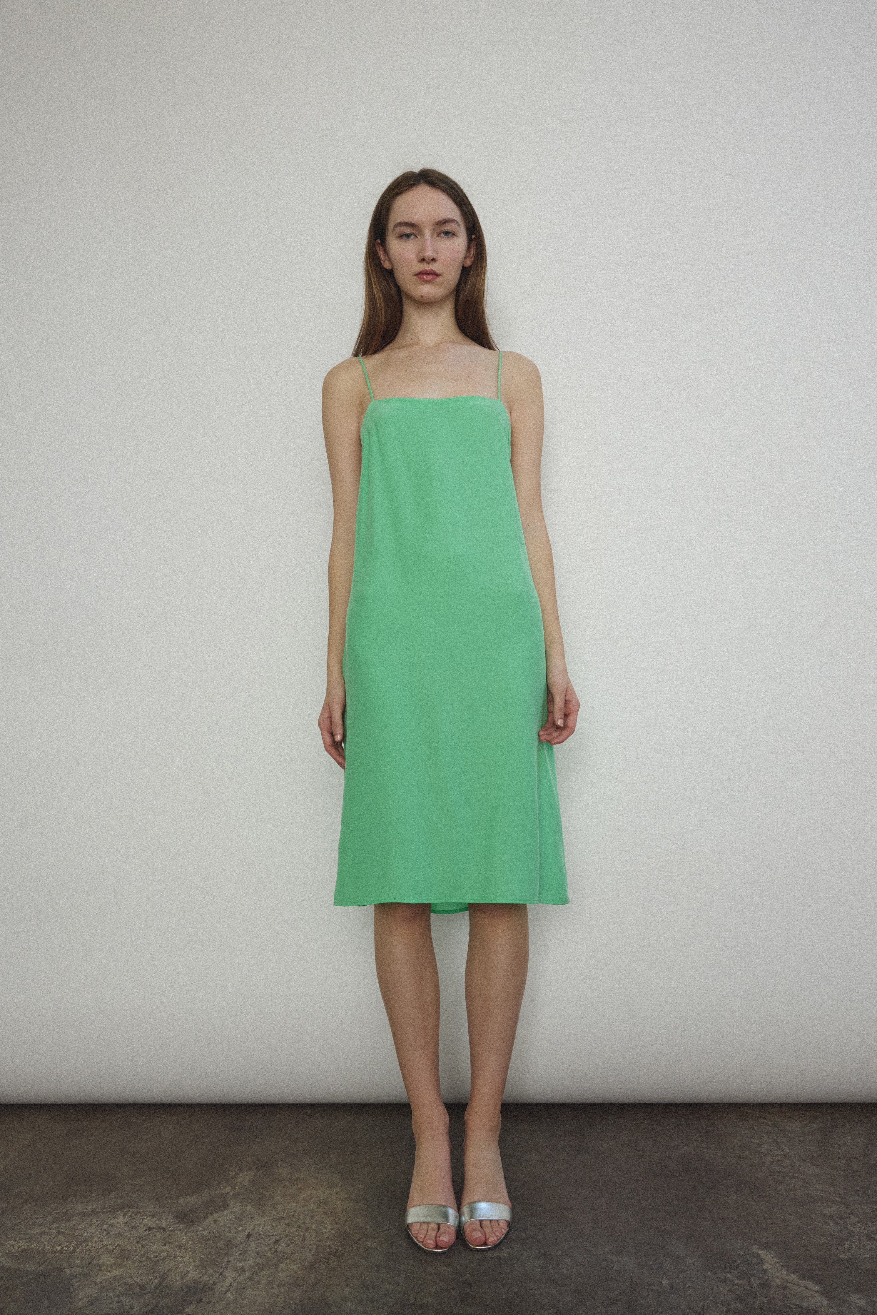 Front view of a model wearing the celadon silk charmeuse Kamperett Short Slip, a midi slip with fixed spaghetti straps.