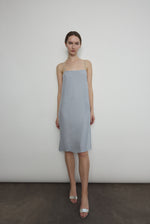 Front view of a model wearing the powder blue silk charmeuse Kamperett Short Slip, a midi slip with fixed spaghetti straps.
