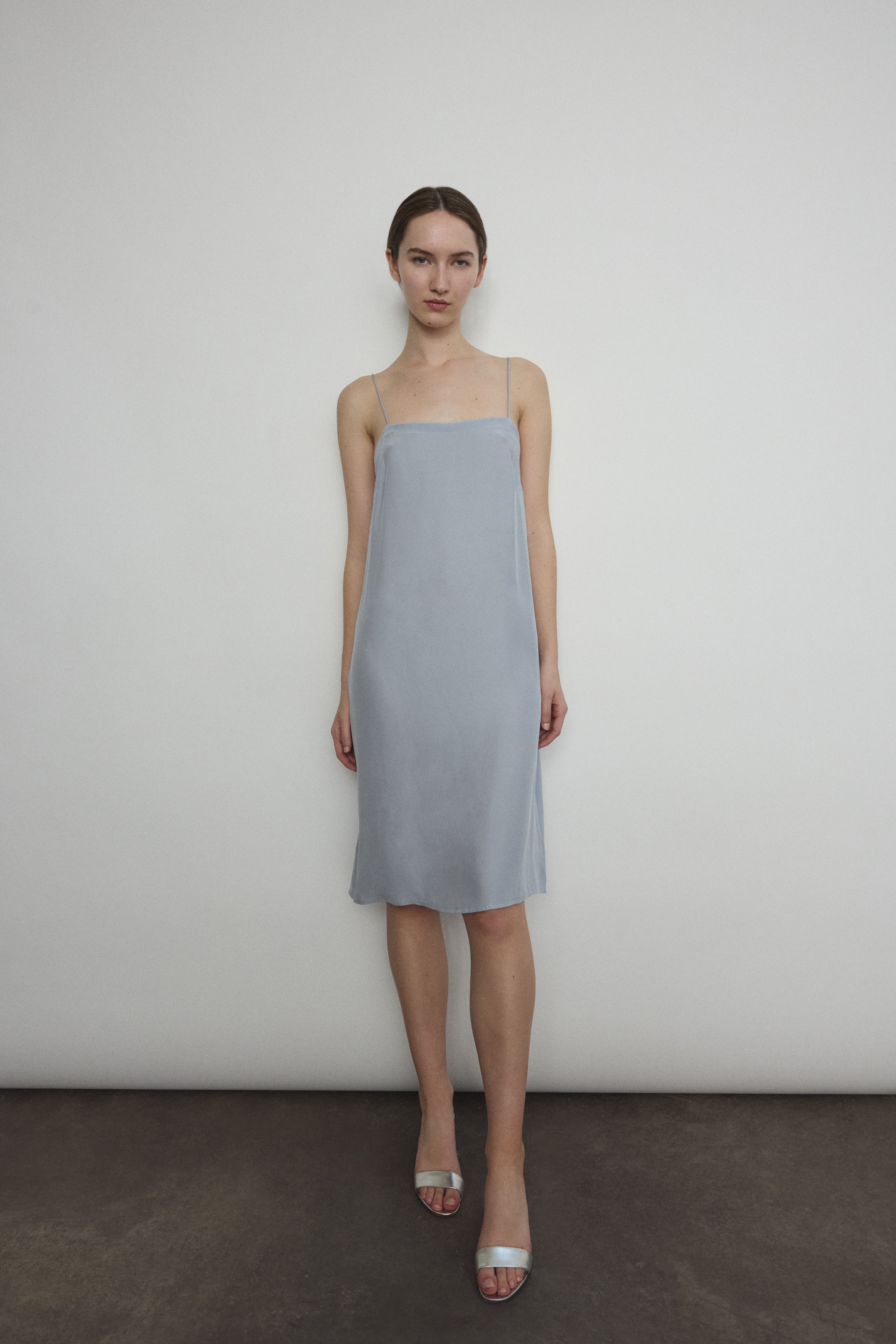 Front view of a model wearing the powder blue silk charmeuse Kamperett Short Slip, a midi slip with fixed spaghetti straps.