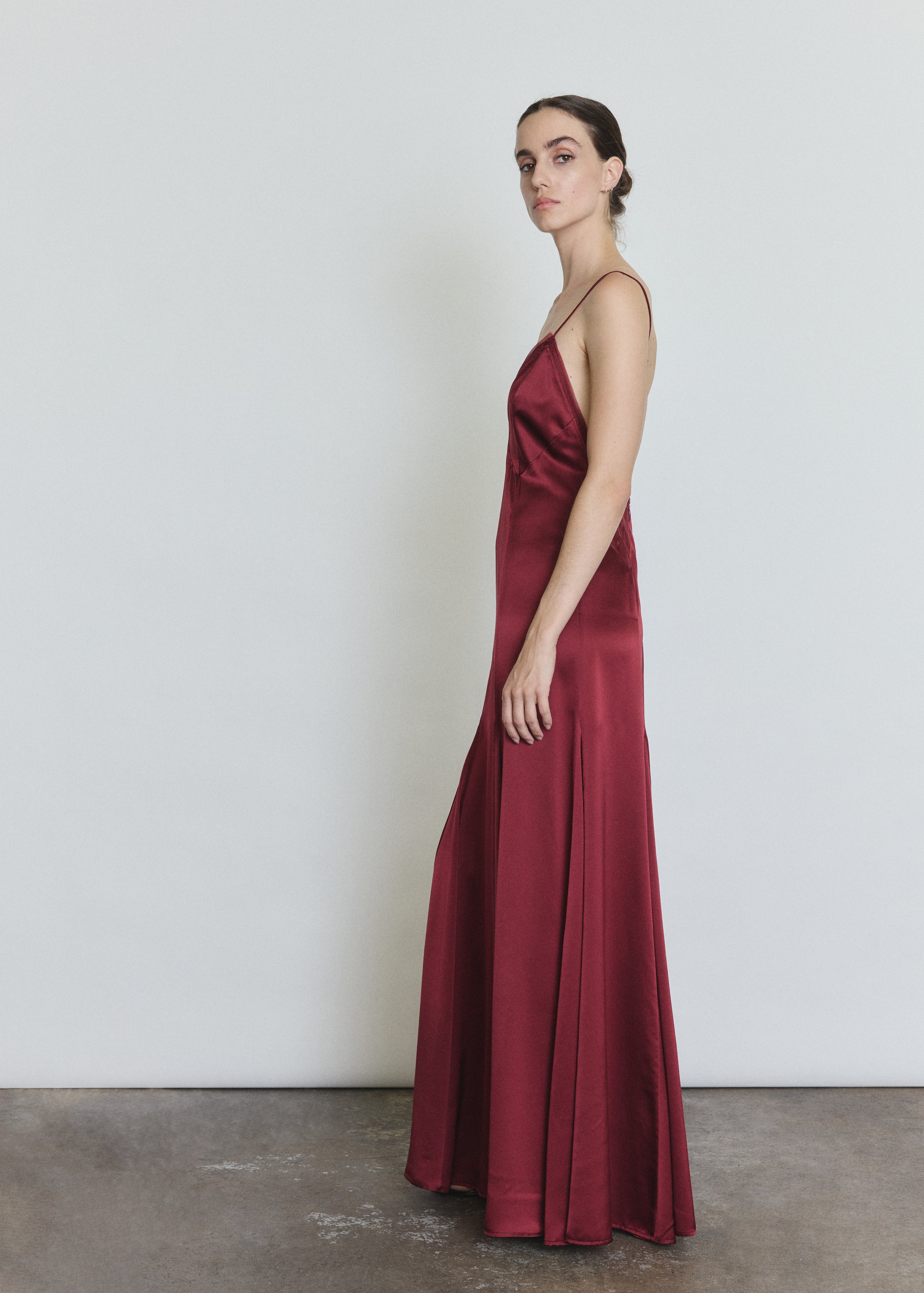 Side view of the bordeaux silk charmeuse Kamperett Simone Slip Dress showing the multi-godet hemline.