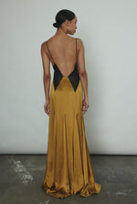 Editorial image of a model wearing the brass silk charmeuse Kamperett Simone Slip Dress, a Deco-inspired V-neck gown with sheer diamond panels.
