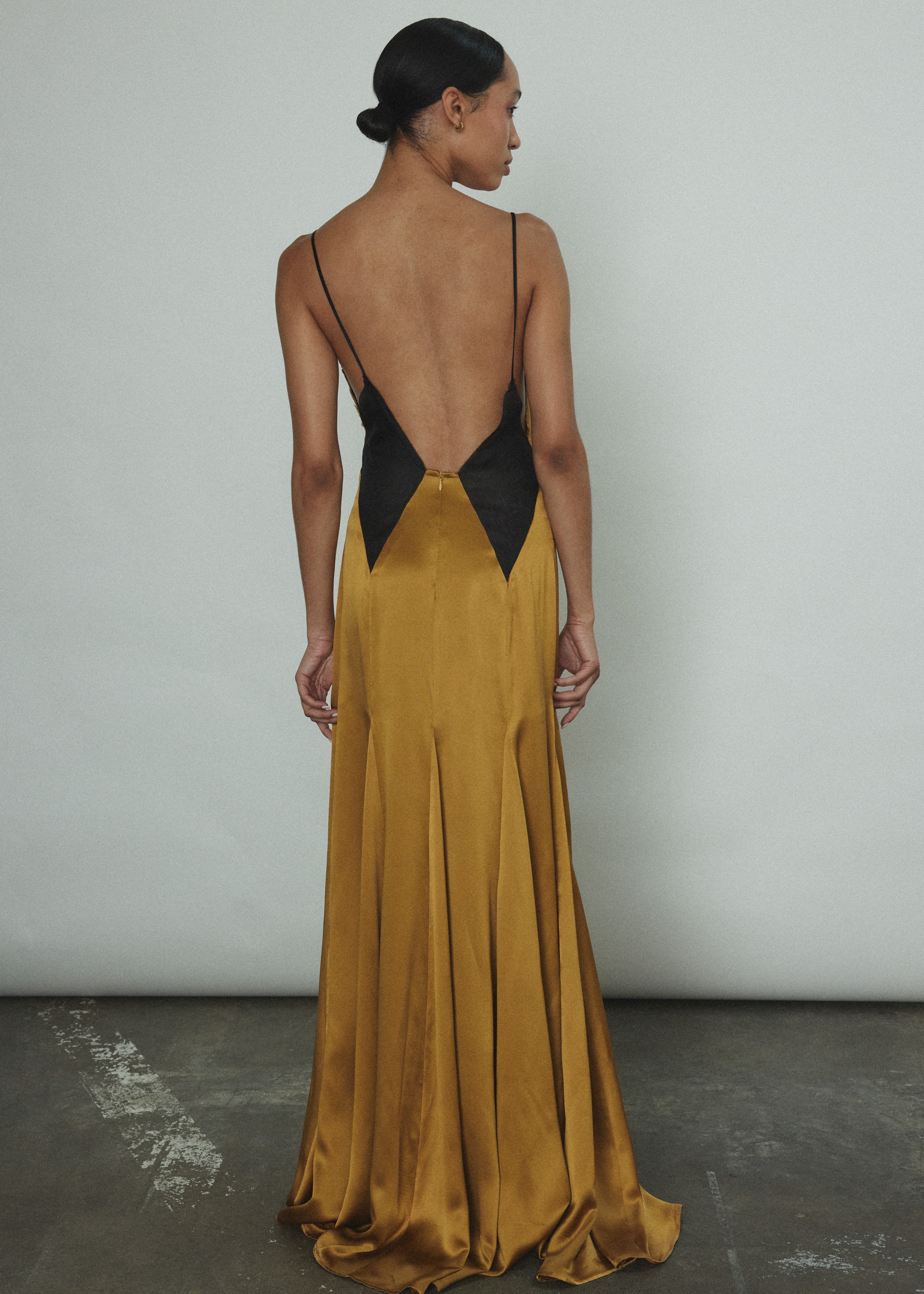 Editorial image of a model wearing the brass silk charmeuse Kamperett Simone Slip Dress, a Deco-inspired V-neck gown with sheer diamond panels.