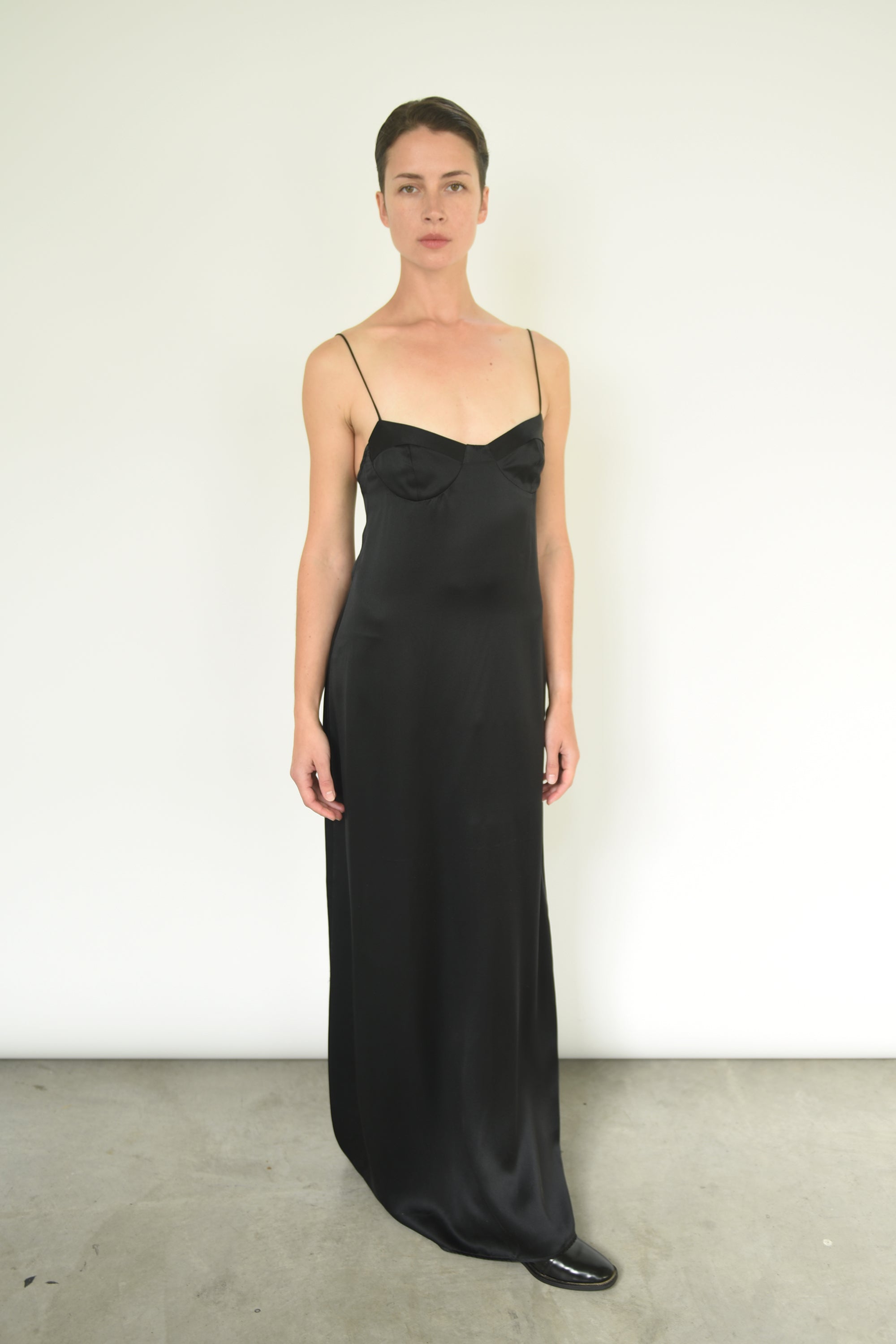 Front view of a model wearing the black silk charmeuse Kamperett Sloan Slip, a maxi-length minimal slip with corded straps.