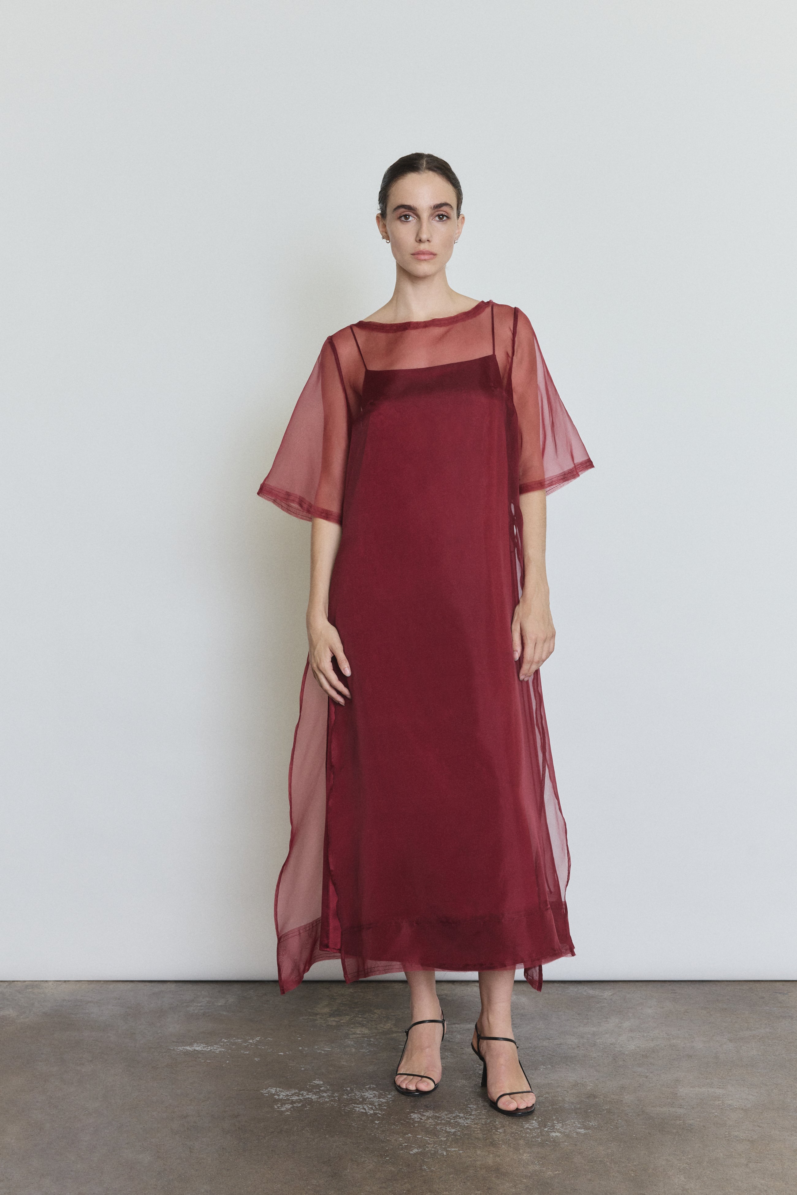 Front view of a model wearing the bordeaux silk organza Kamperett Thea Sheath Dress, a midi sheath with raw-edge neckline and side ties.