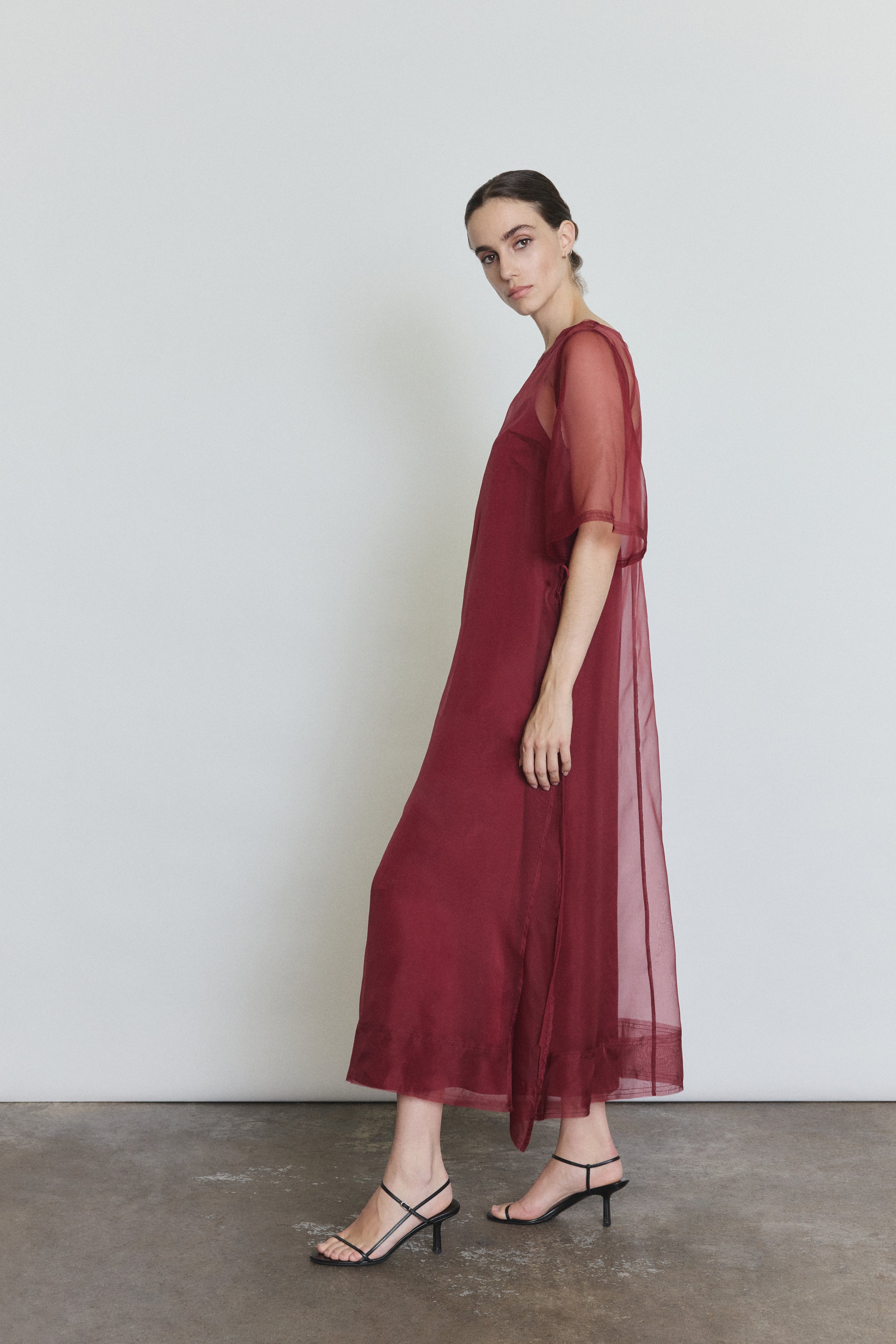 Side view of the bordeaux silk organza Kamperett Thea Sheath Dress showing the open side seams with self corded ties.