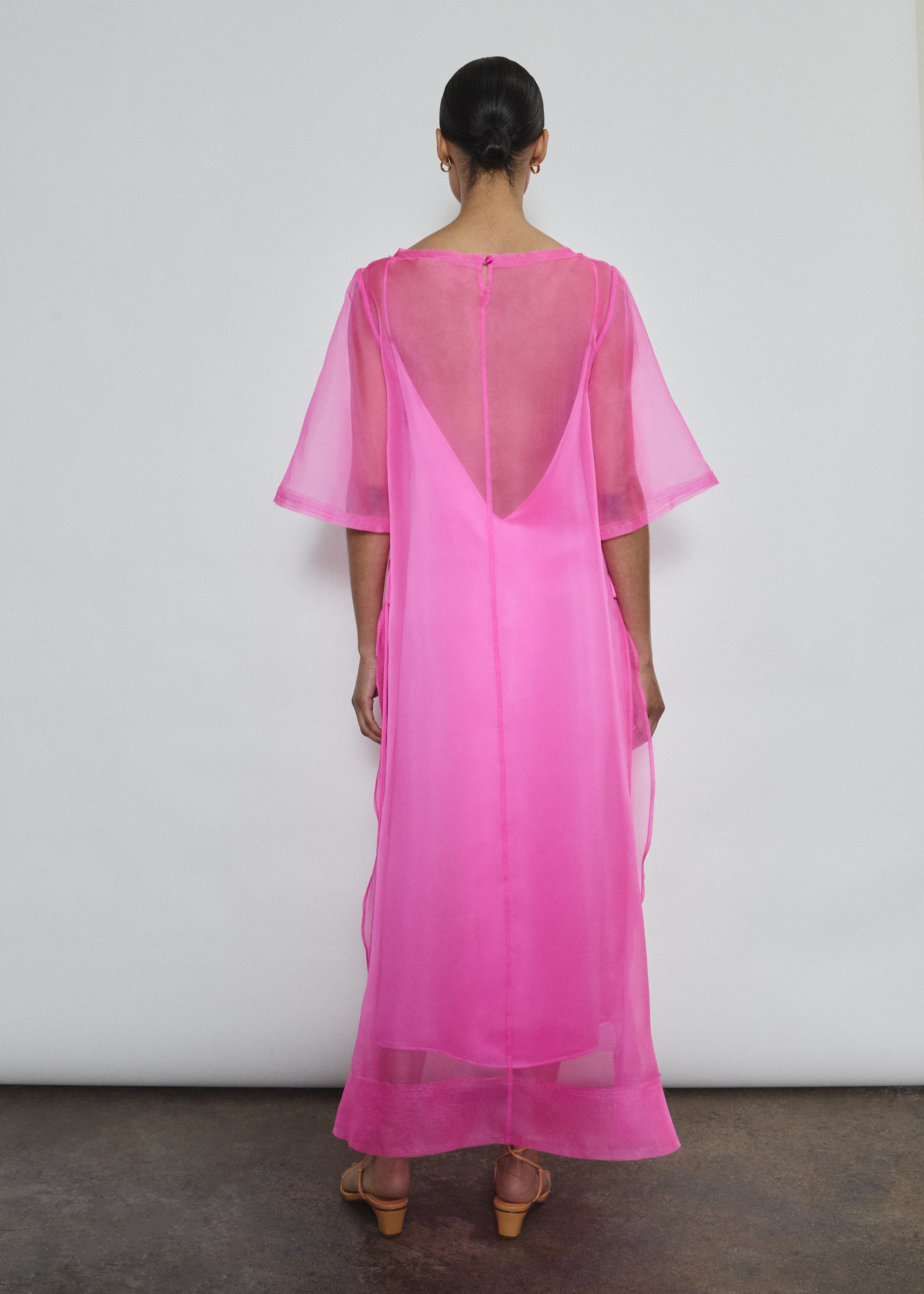 Rear view of hot pink Thea Sheath Dress in sheer silk organza. Open side seams and wide hem facing reveal architectural construction. Ethically made in California.